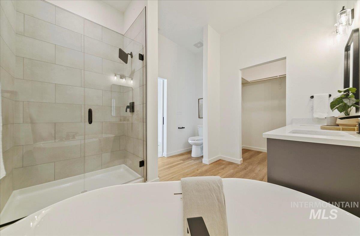 Full bathroom with a walk in closet, a stall shower, double vanity, a freestanding bath, and light wood finished floors