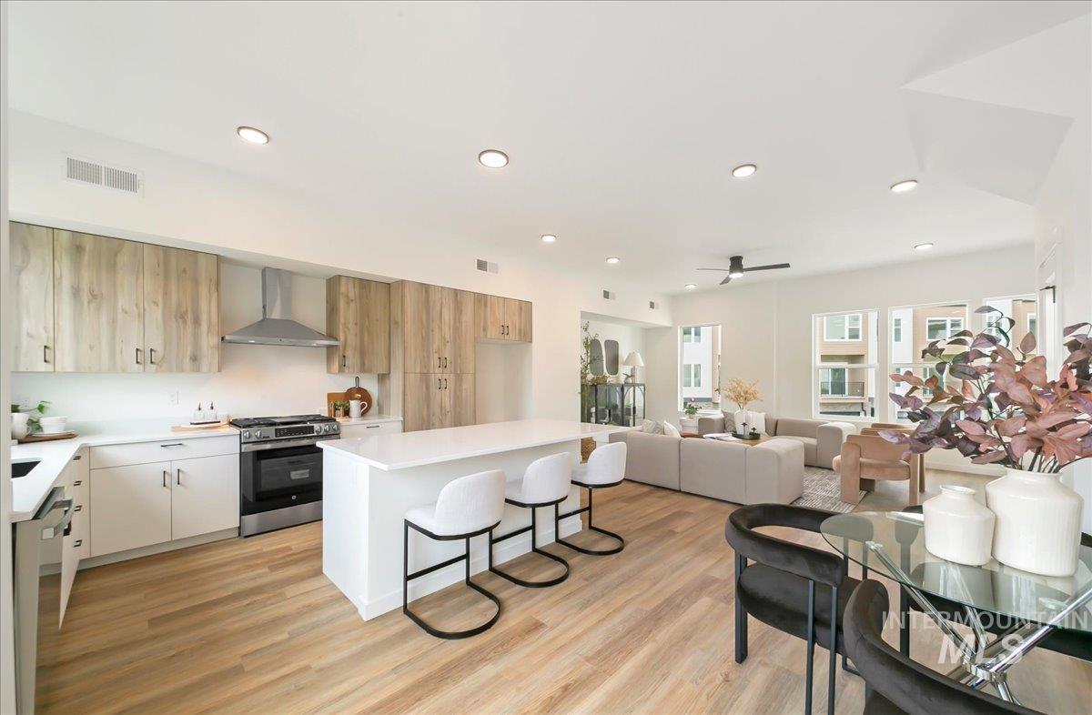 Kitchen featuring a breakfast bar area, appliances with stainless steel finishes, modern cabinets, a center island, and wall chimney range hood
