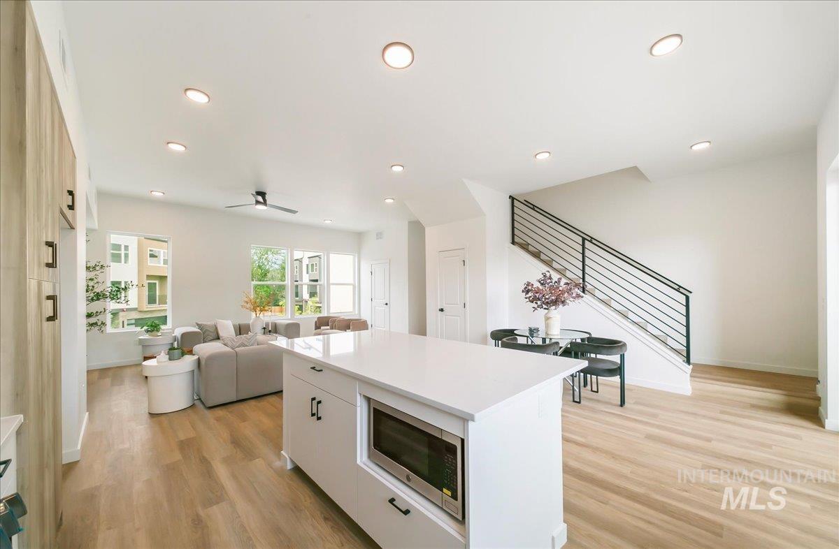 Kitchen featuring stainless steel microwave, a center island, white cabinetry, light wood-style floors, and recessed lighting