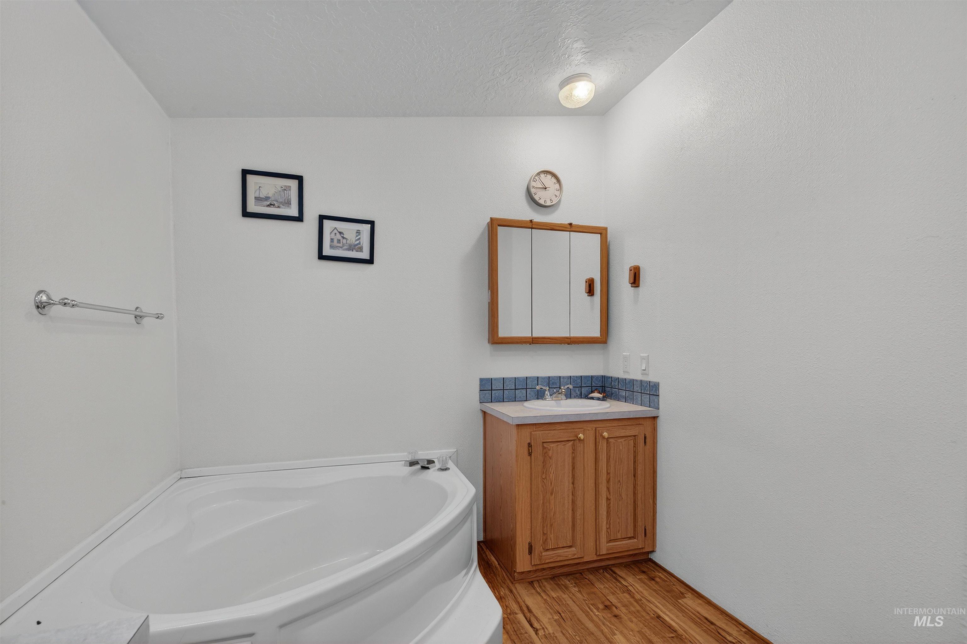 Bathroom featuring a garden tub, light wood-style floors, vanity, and a textured ceiling