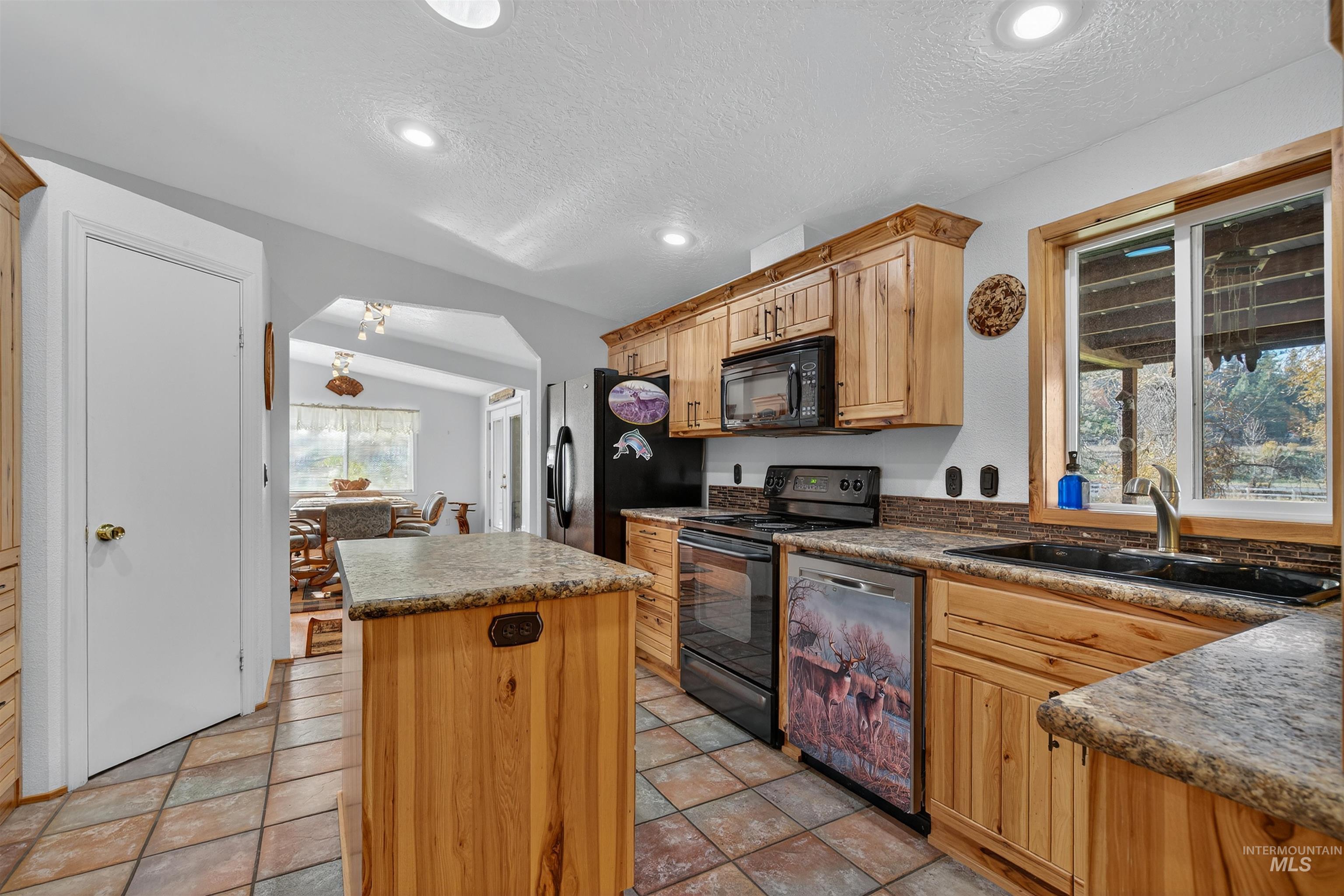 Kitchen with a center island, black appliances, arched walkways, vaulted ceiling, and a textured ceiling