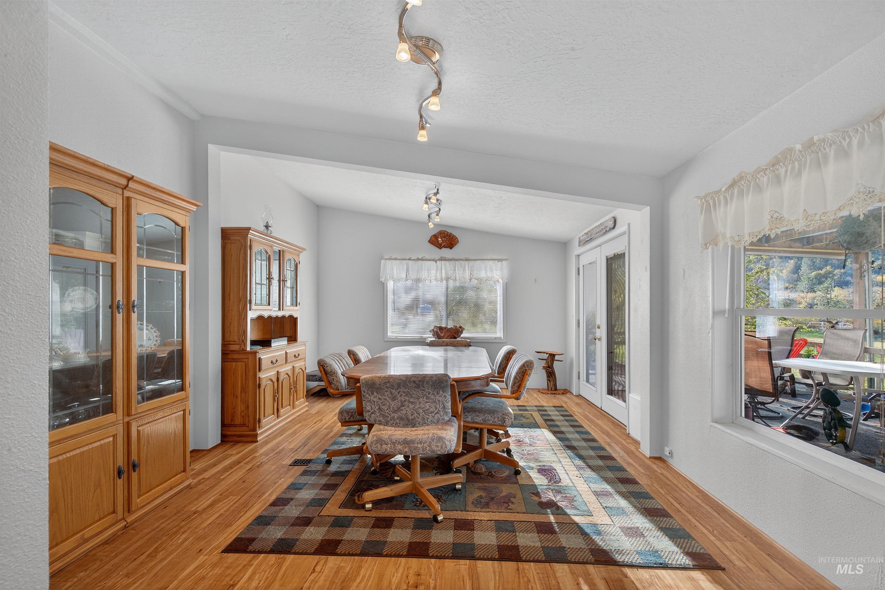 Dining room with light wood-style flooring, track lighting, a textured ceiling, and lofted ceiling