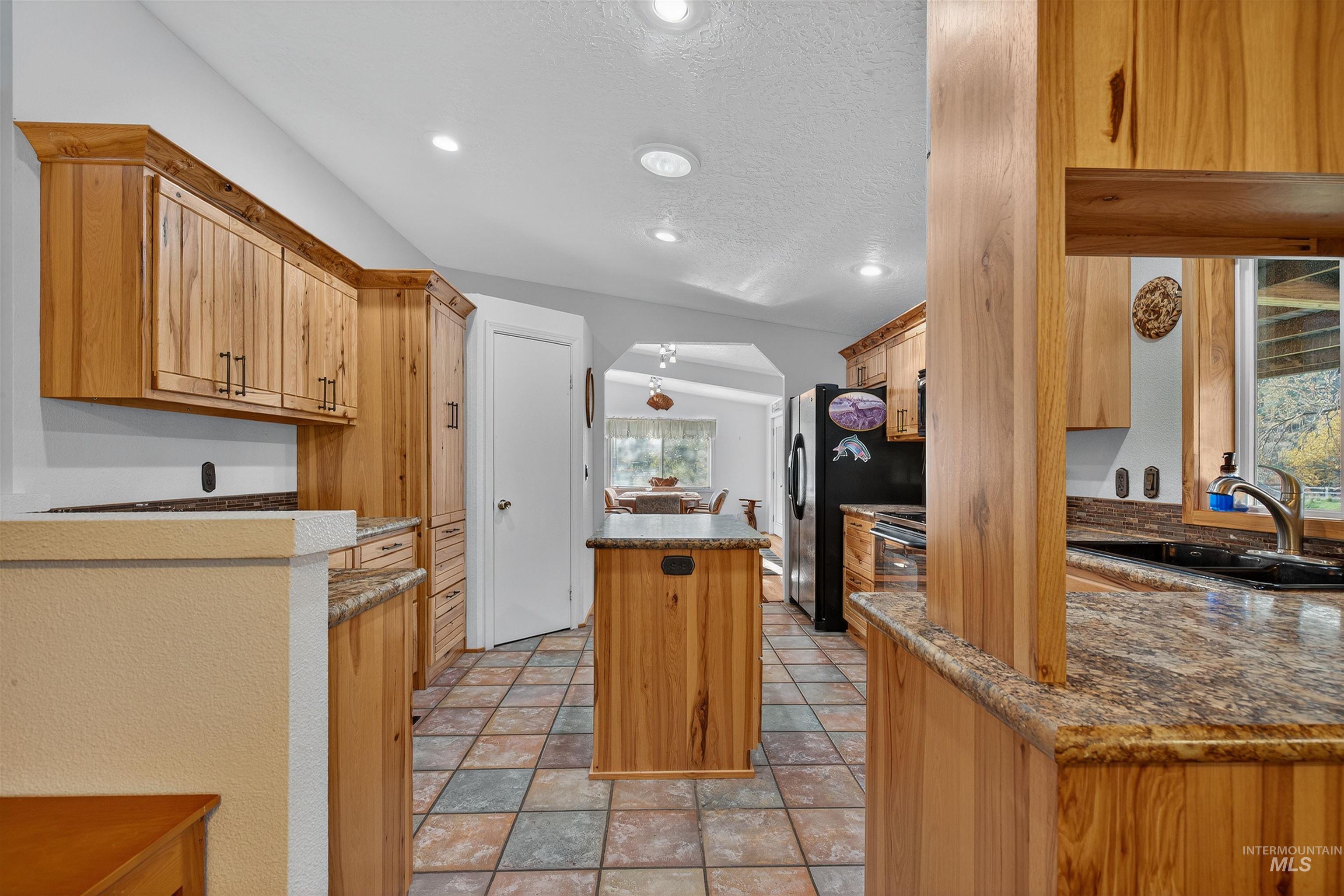 Kitchen with a kitchen island, arched walkways, a textured ceiling, black refrigerator with ice dispenser, and recessed lighting