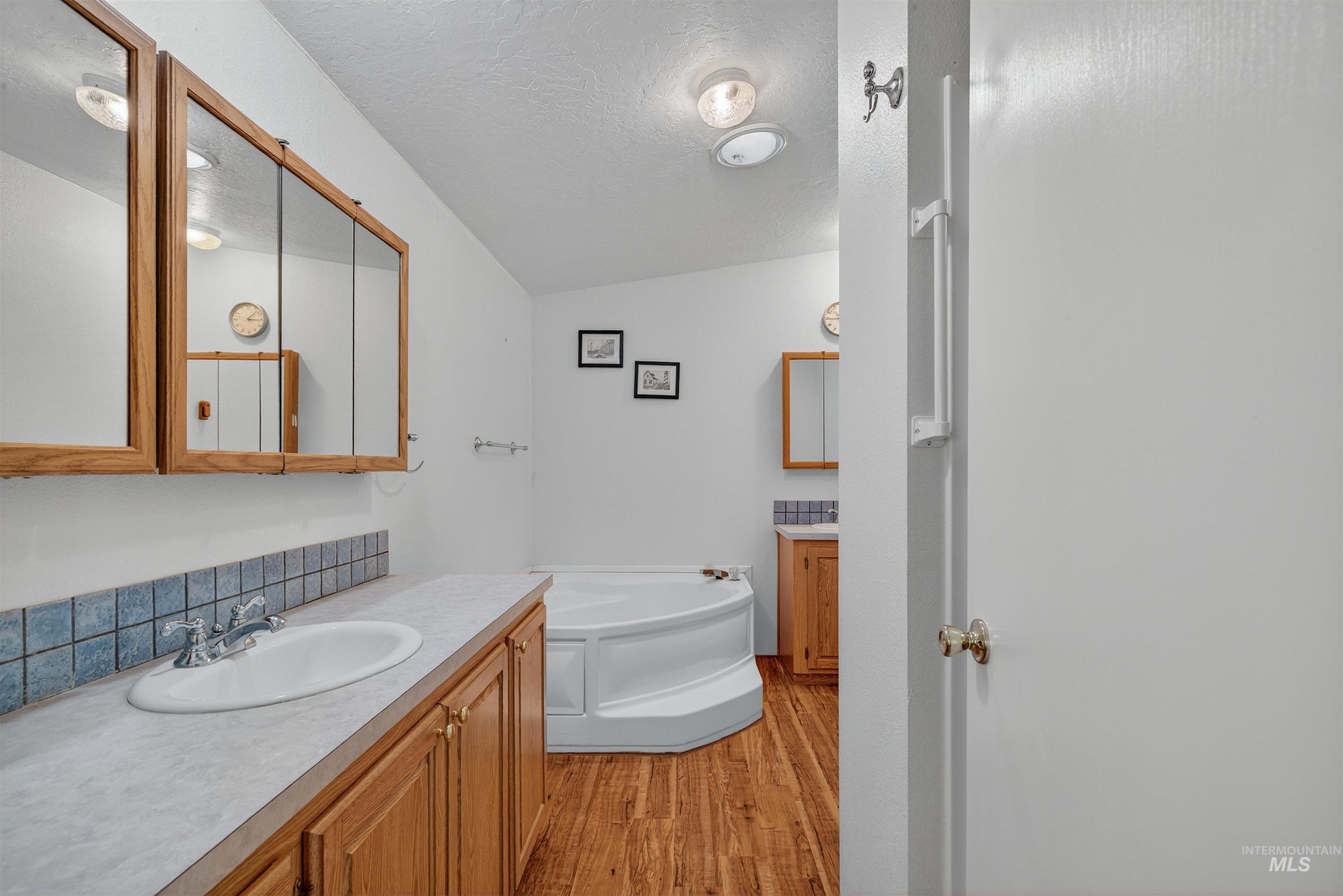 Full bathroom featuring vanity, a textured ceiling, a garden tub, and light wood-type flooring