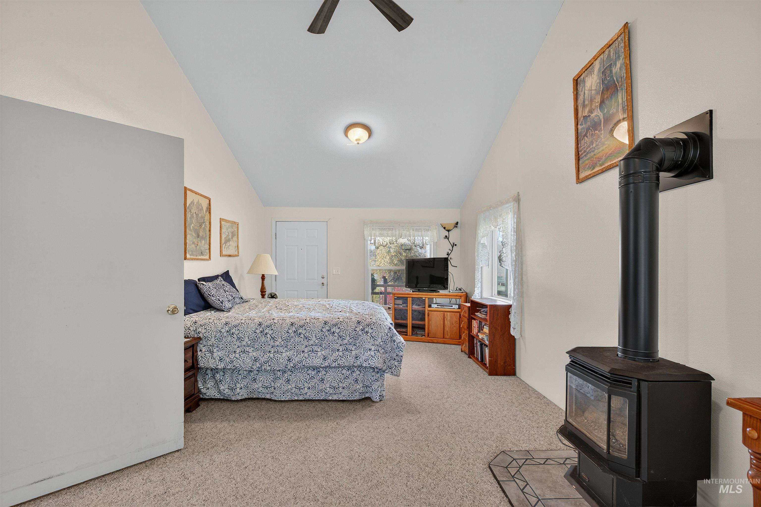 Bedroom with a wood stove, vaulted ceiling, light carpet, and ceiling fan
