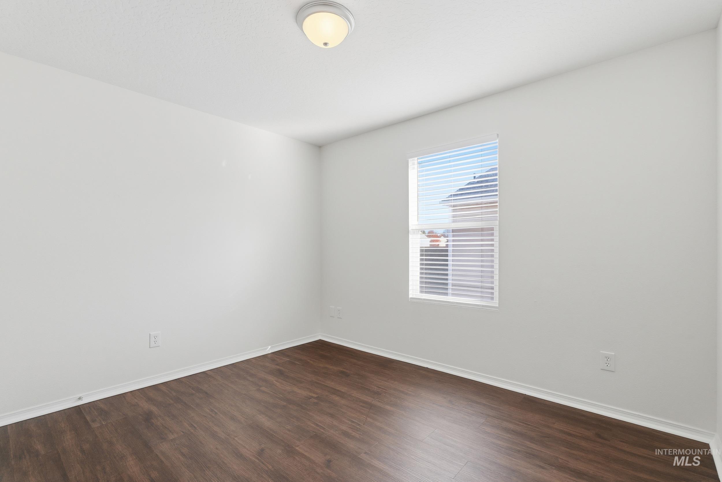 Empty room with dark wood-type flooring and baseboards