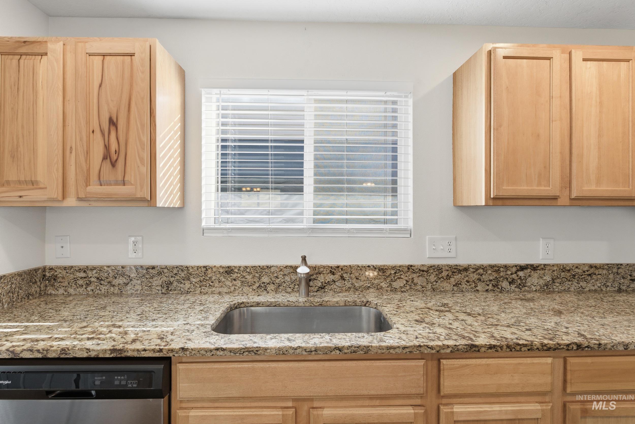 Kitchen with light brown cabinets, light stone counters, and stainless steel dishwasher