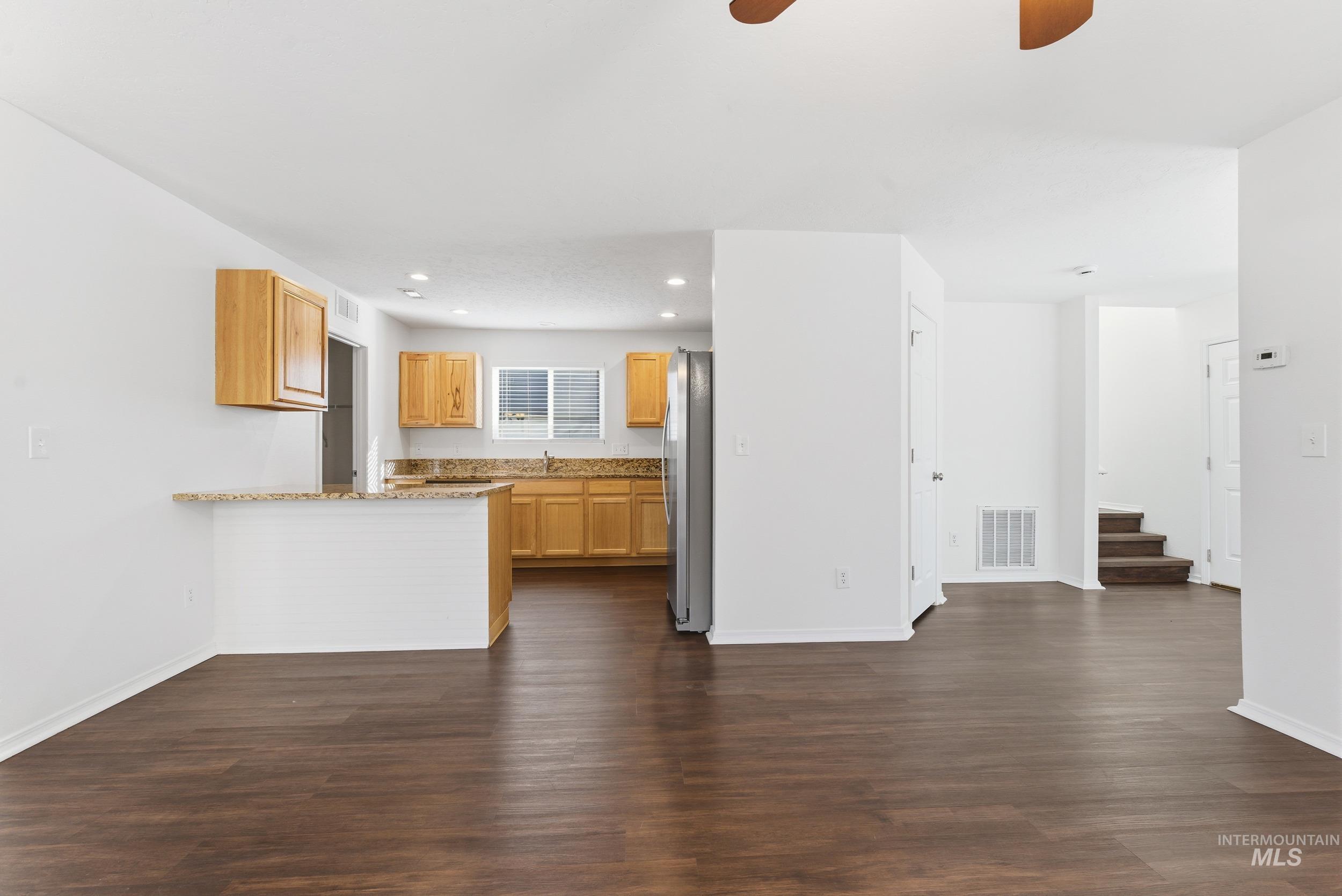 Kitchen with a peninsula, light brown cabinets, dark wood-type flooring, light stone counters, and recessed lighting