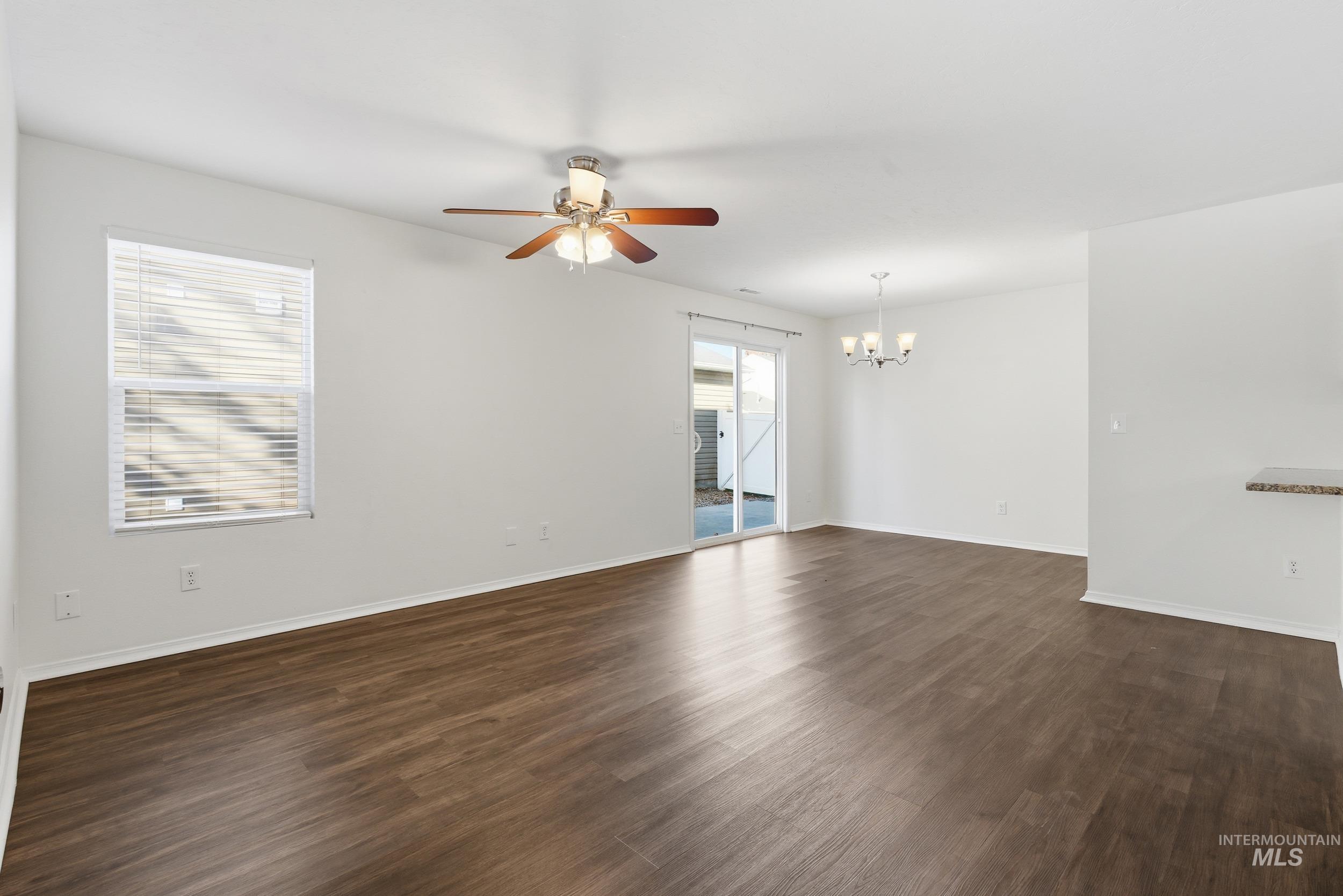 Spare room featuring dark wood-style flooring, healthy amount of natural light, a ceiling fan, and a chandelier