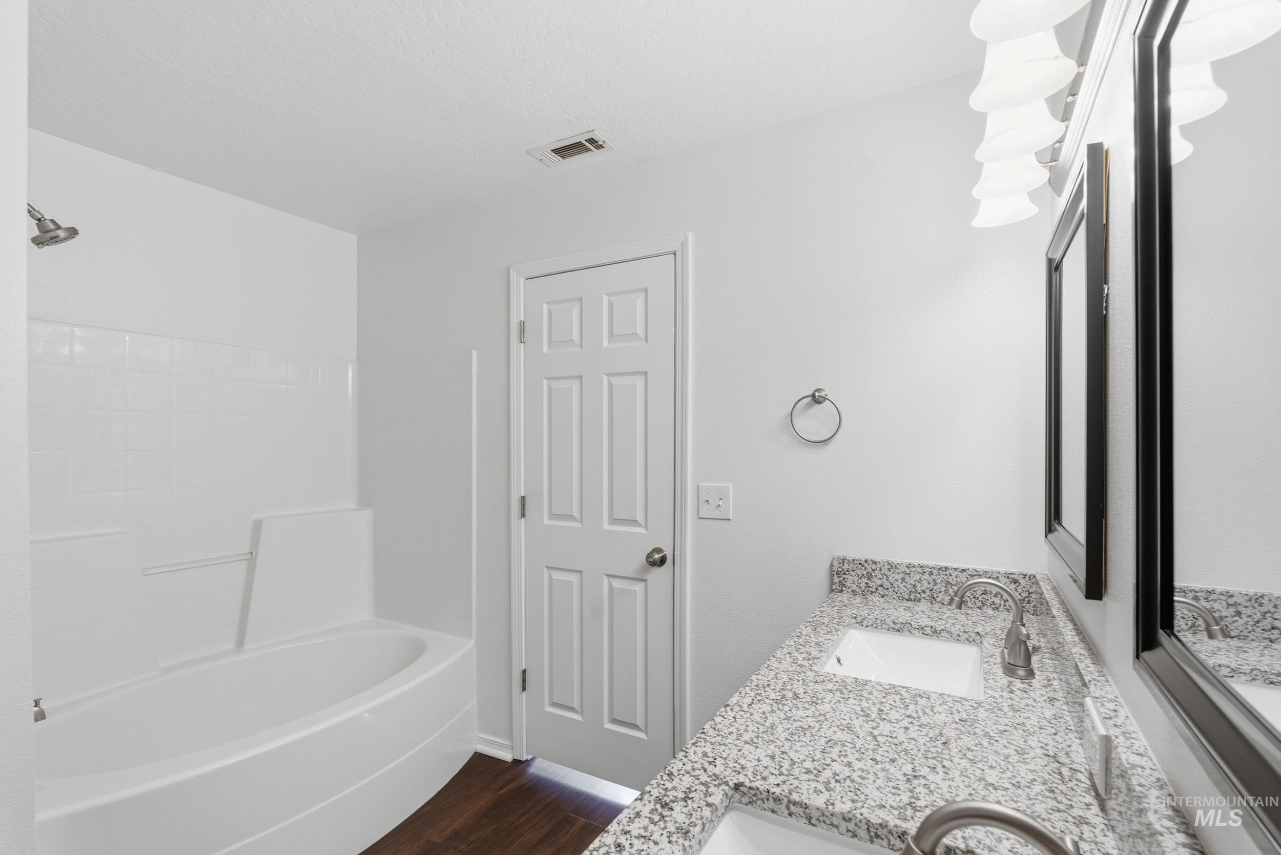 Full bath with double vanity, dark wood-style flooring, and bathing tub / shower combination