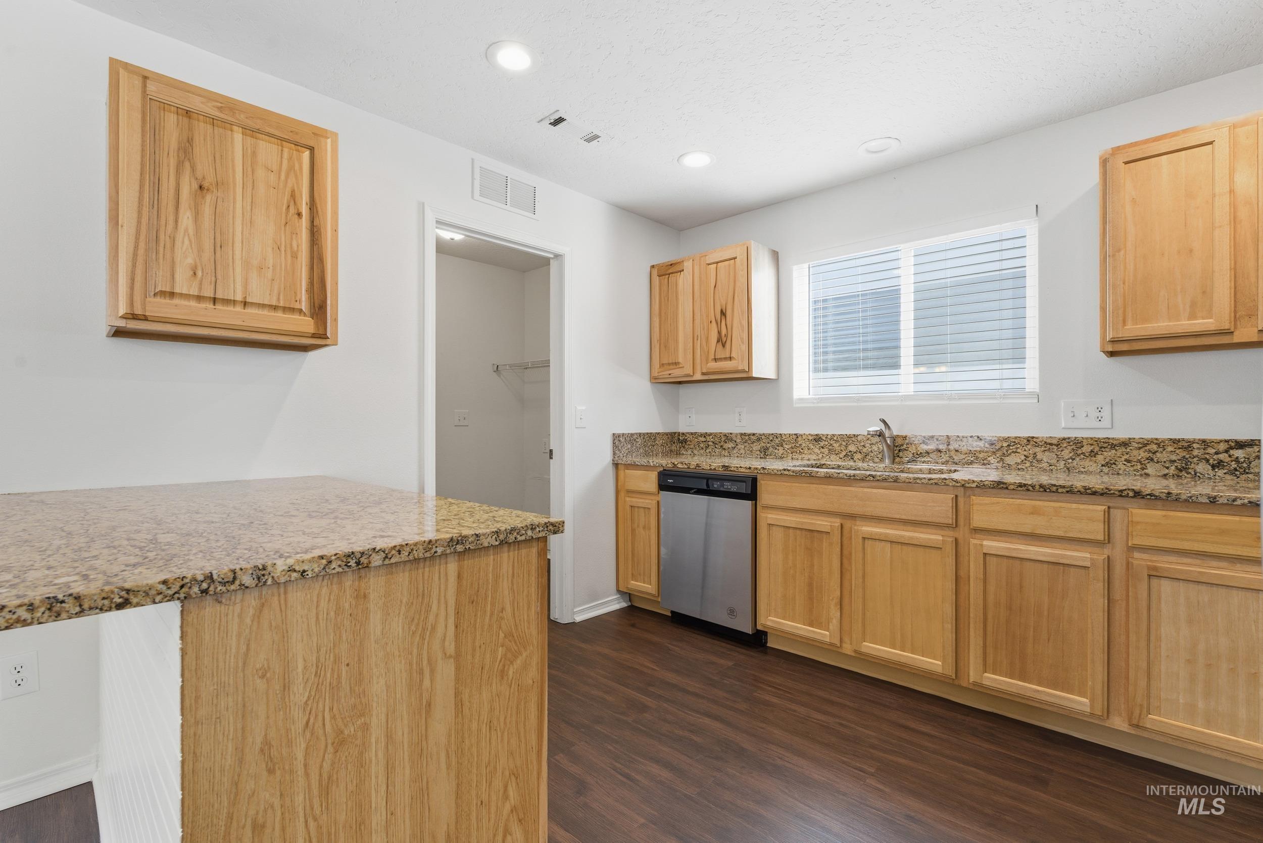 Kitchen with light stone countertops, light brown cabinets, dark wood-style flooring, dishwasher, and recessed lighting