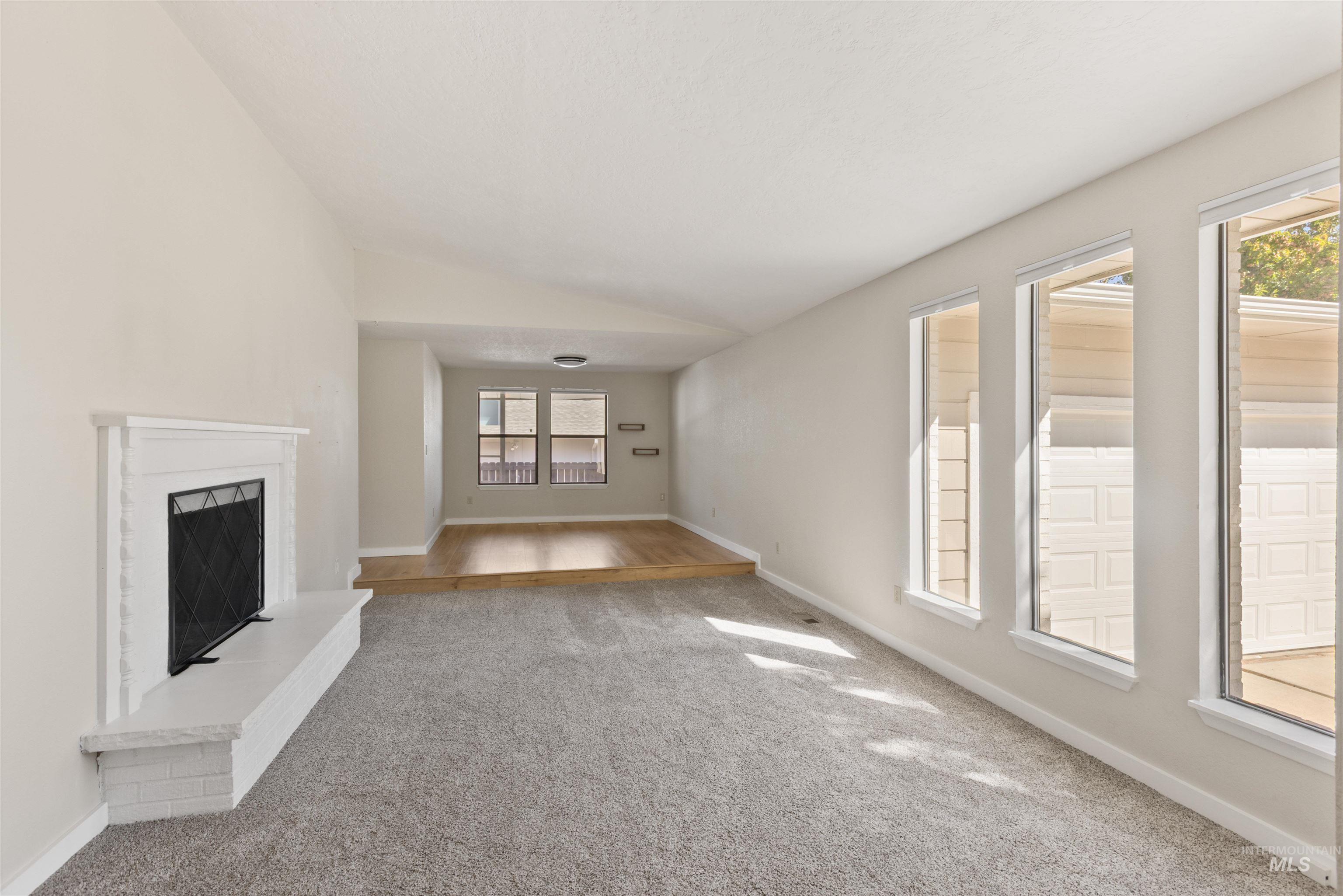 Unfurnished living room with carpet flooring, vaulted ceiling, and a fireplace with raised hearth