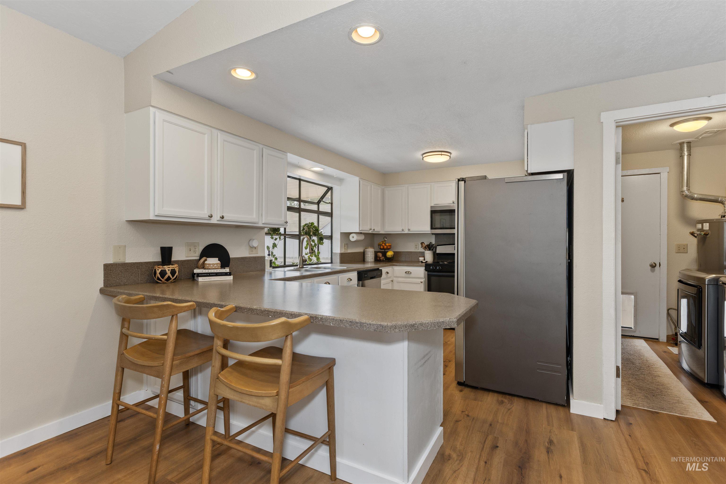 Kitchen featuring appliances with stainless steel finishes, a peninsula, white cabinetry, recessed lighting, and wood finished floors