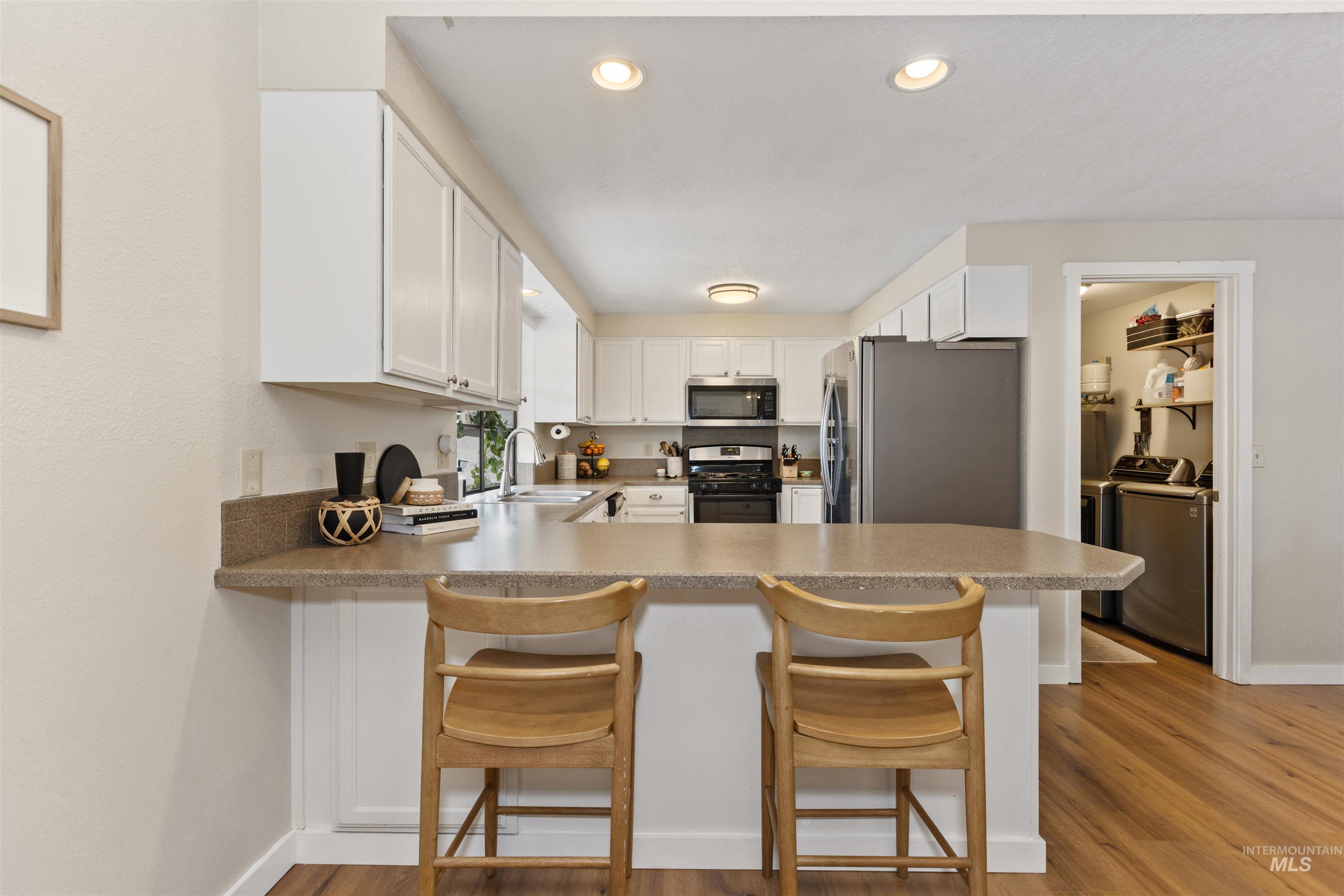 Kitchen featuring appliances with stainless steel finishes, washing machine and dryer, light wood finished floors, a peninsula, and recessed lighting