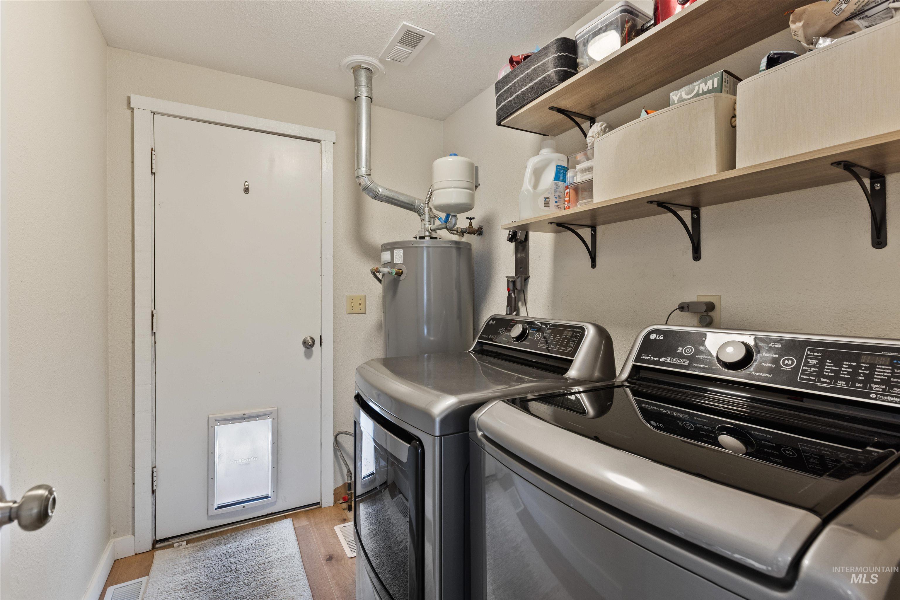 Laundry area with washing machine and clothes dryer, light wood-type flooring, electric water heater, and a textured ceiling