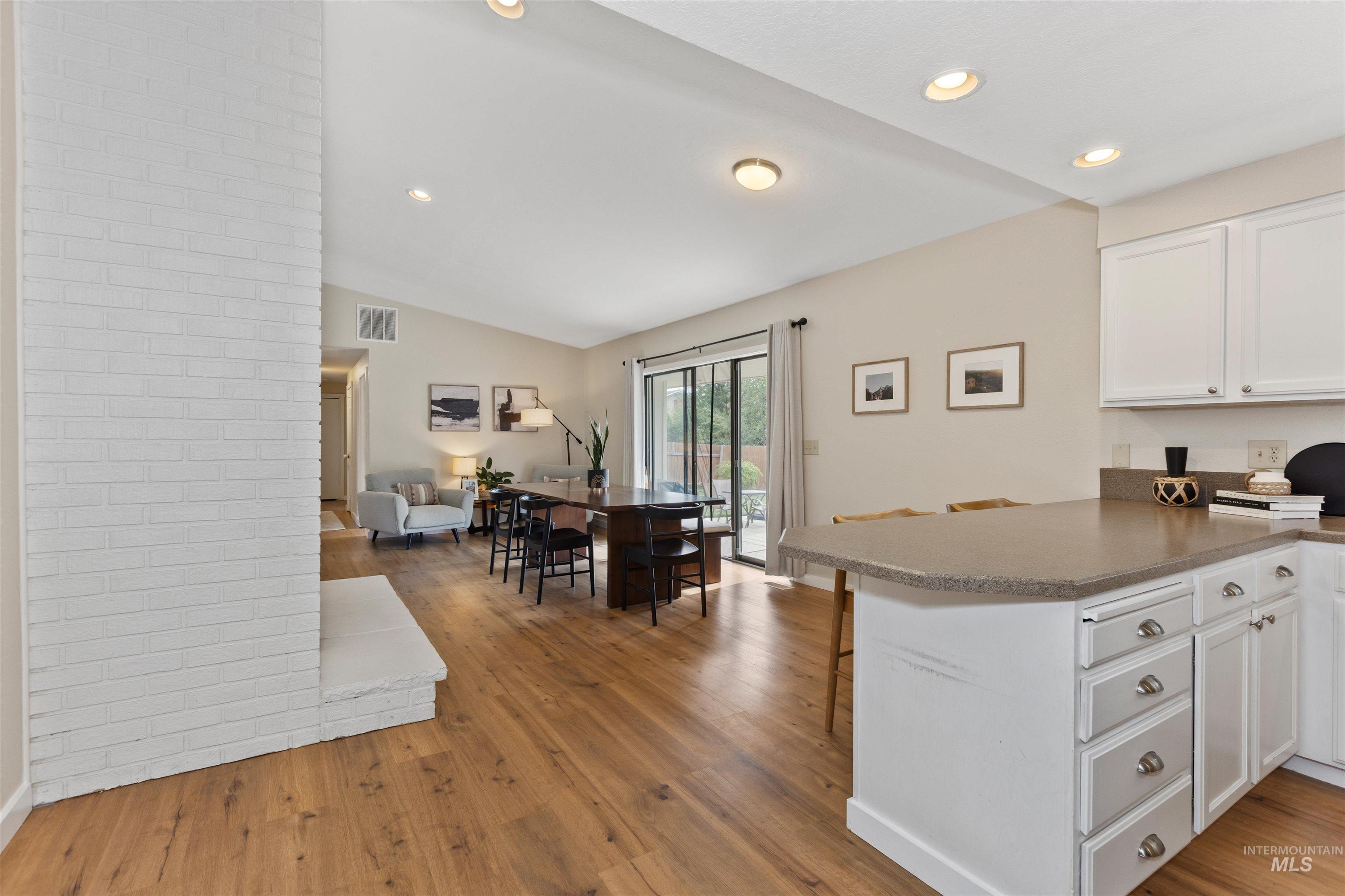 Kitchen featuring wood finished floors, recessed lighting, white cabinetry, vaulted ceiling, and open floor plan