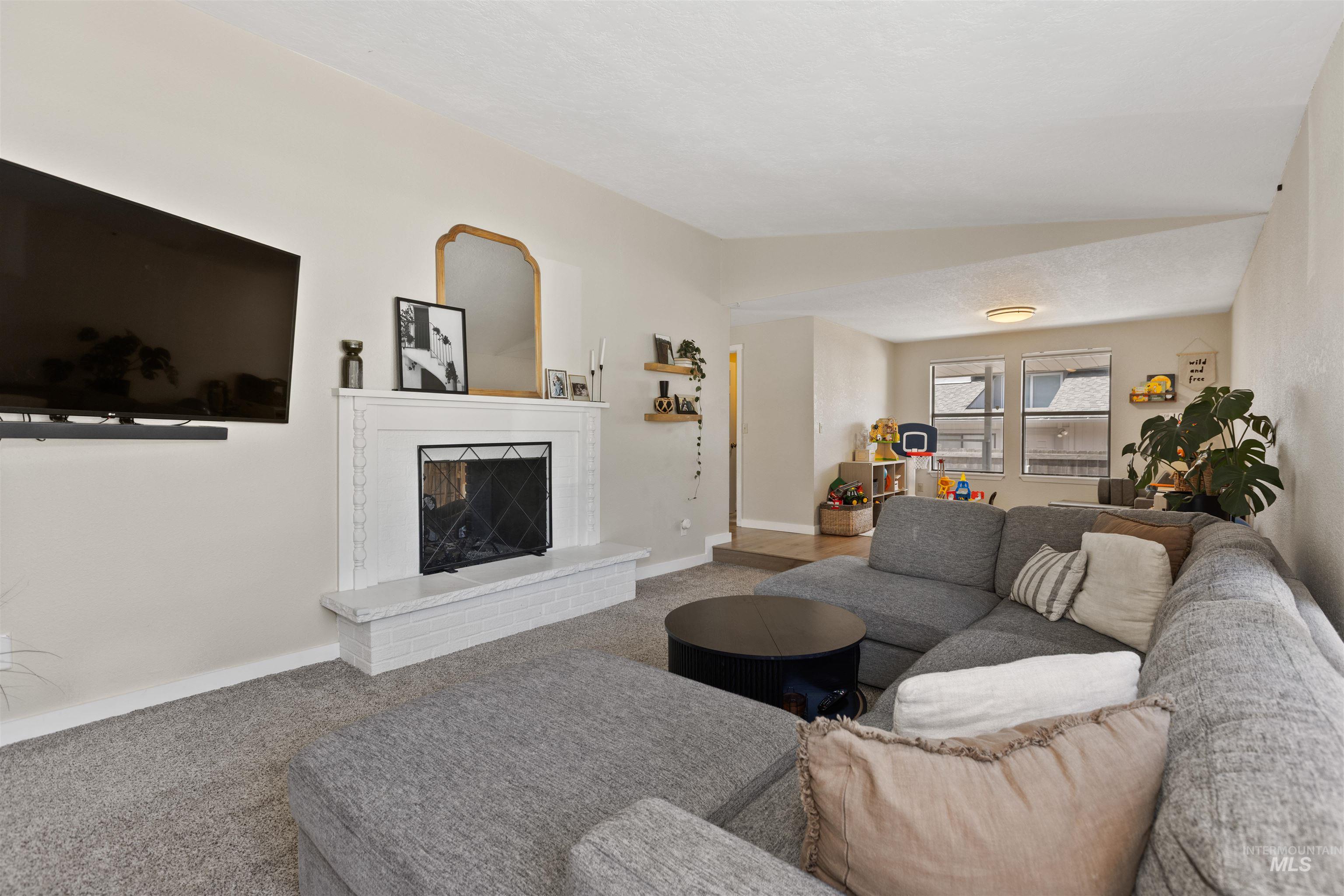 Living area with carpet floors, a brick fireplace, and lofted ceiling