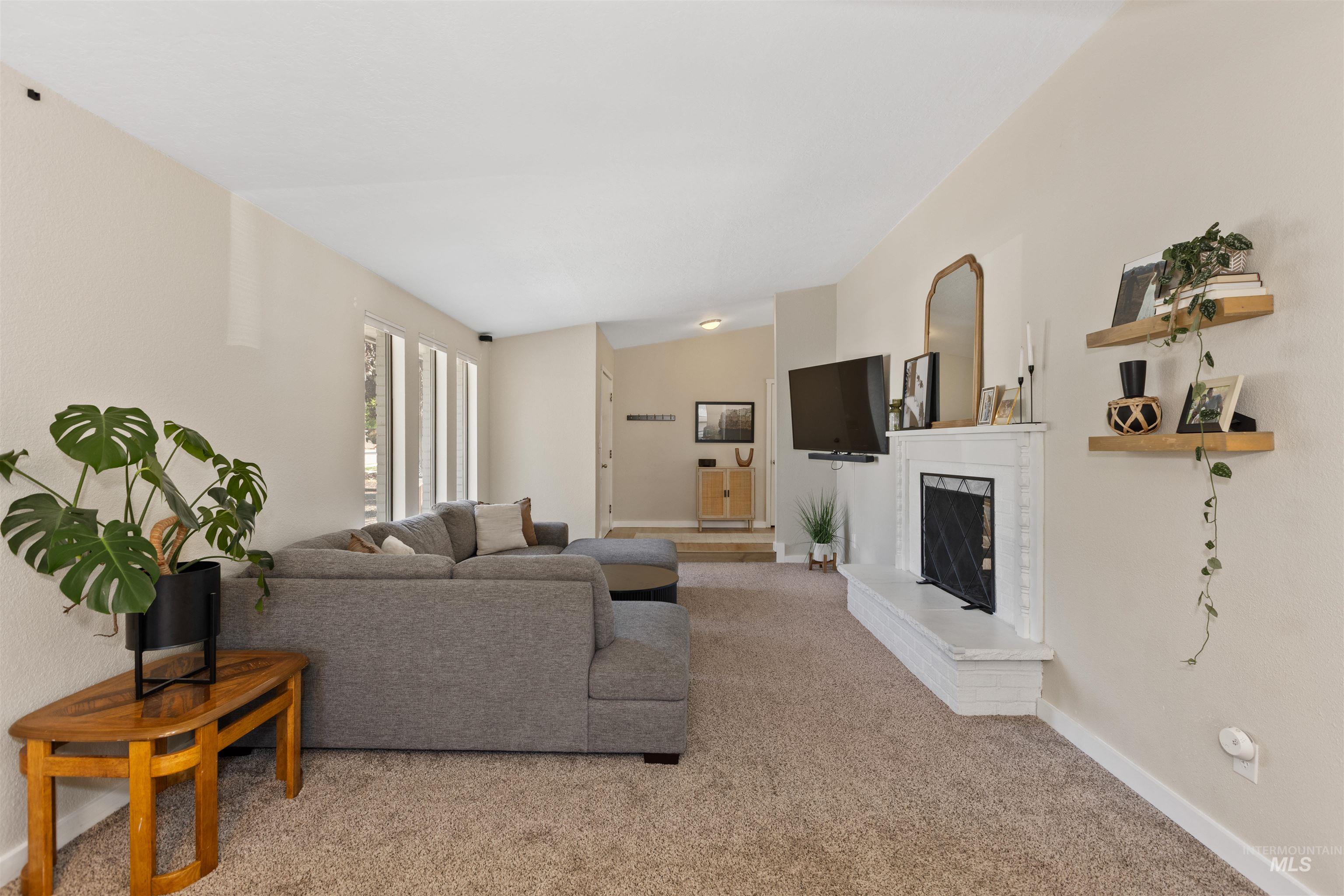 Carpeted living area featuring a fireplace with raised hearth and baseboards