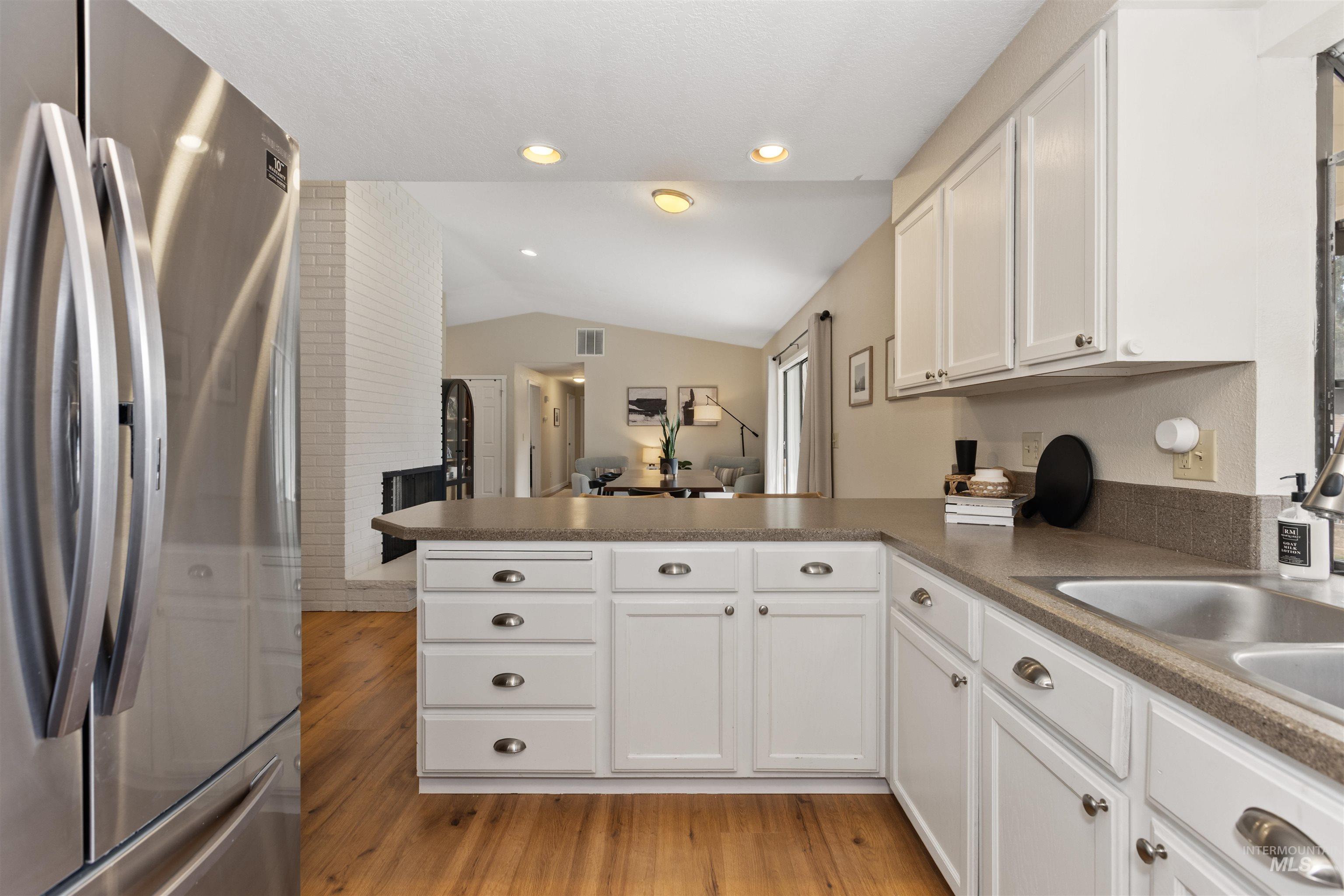 Kitchen featuring freestanding refrigerator, a peninsula, vaulted ceiling, light wood-style flooring, and white cabinetry