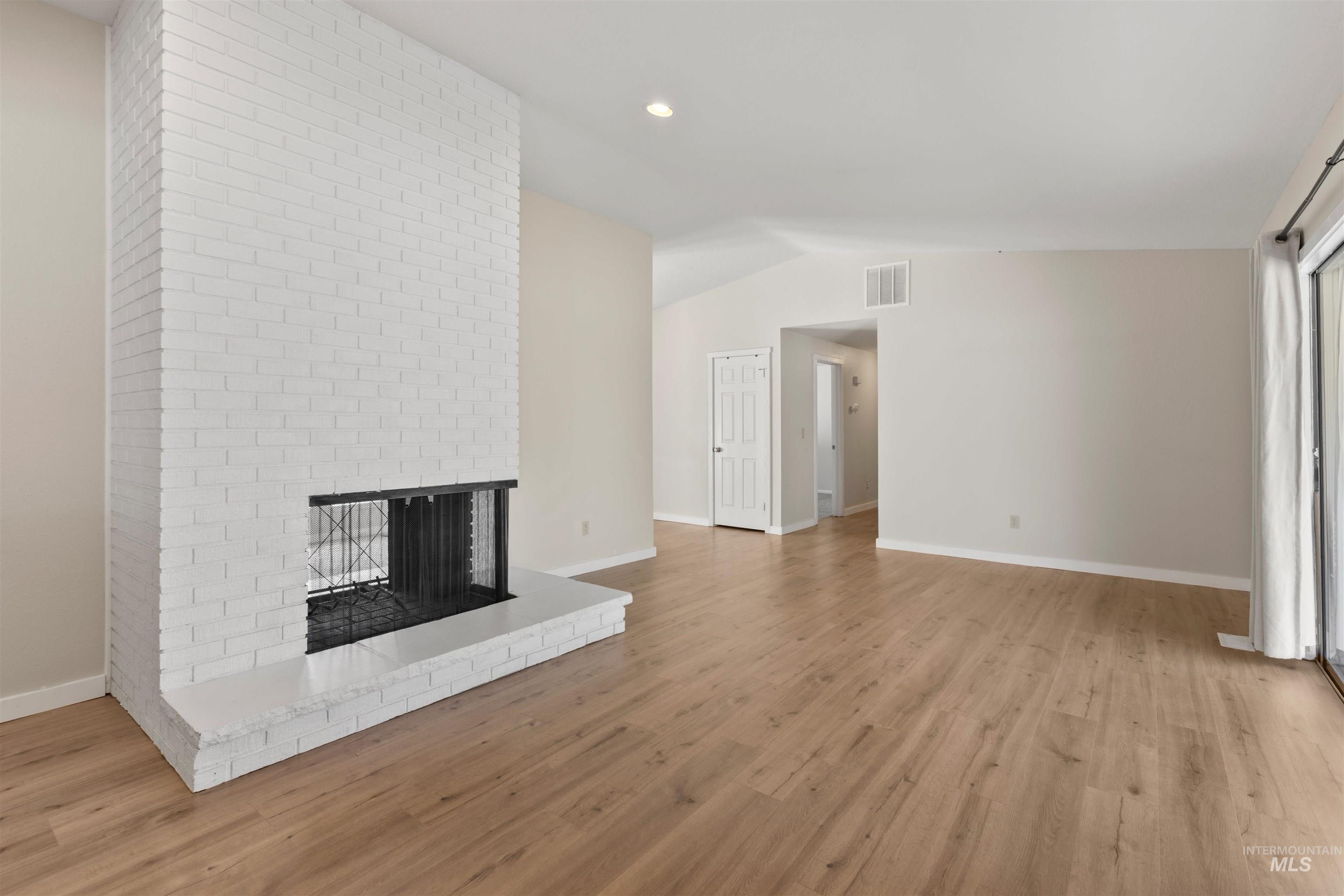Unfurnished living room with a fireplace, vaulted ceiling, light wood finished floors, and recessed lighting