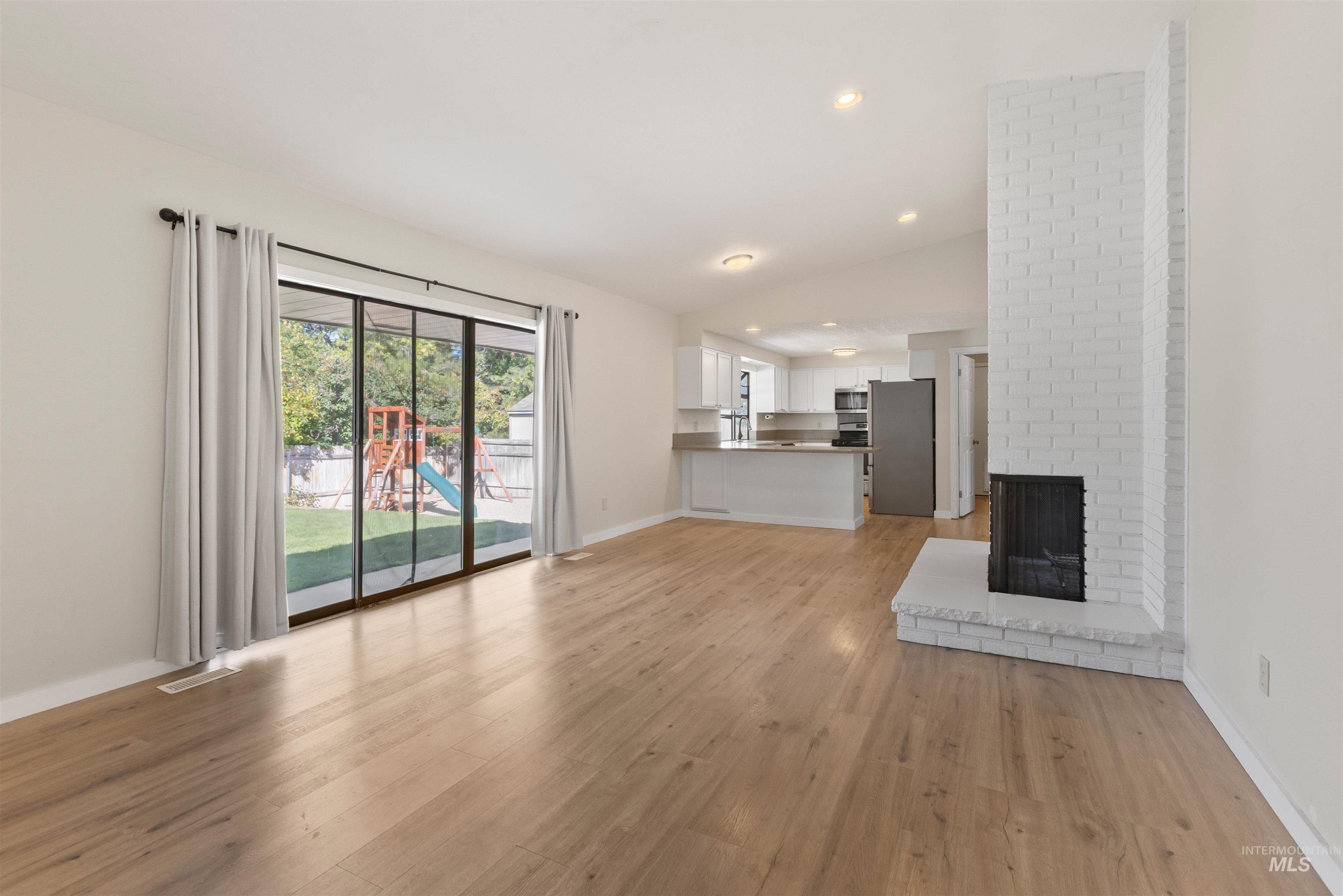 Unfurnished living room with light wood finished floors, lofted ceiling, a brick fireplace, and recessed lighting