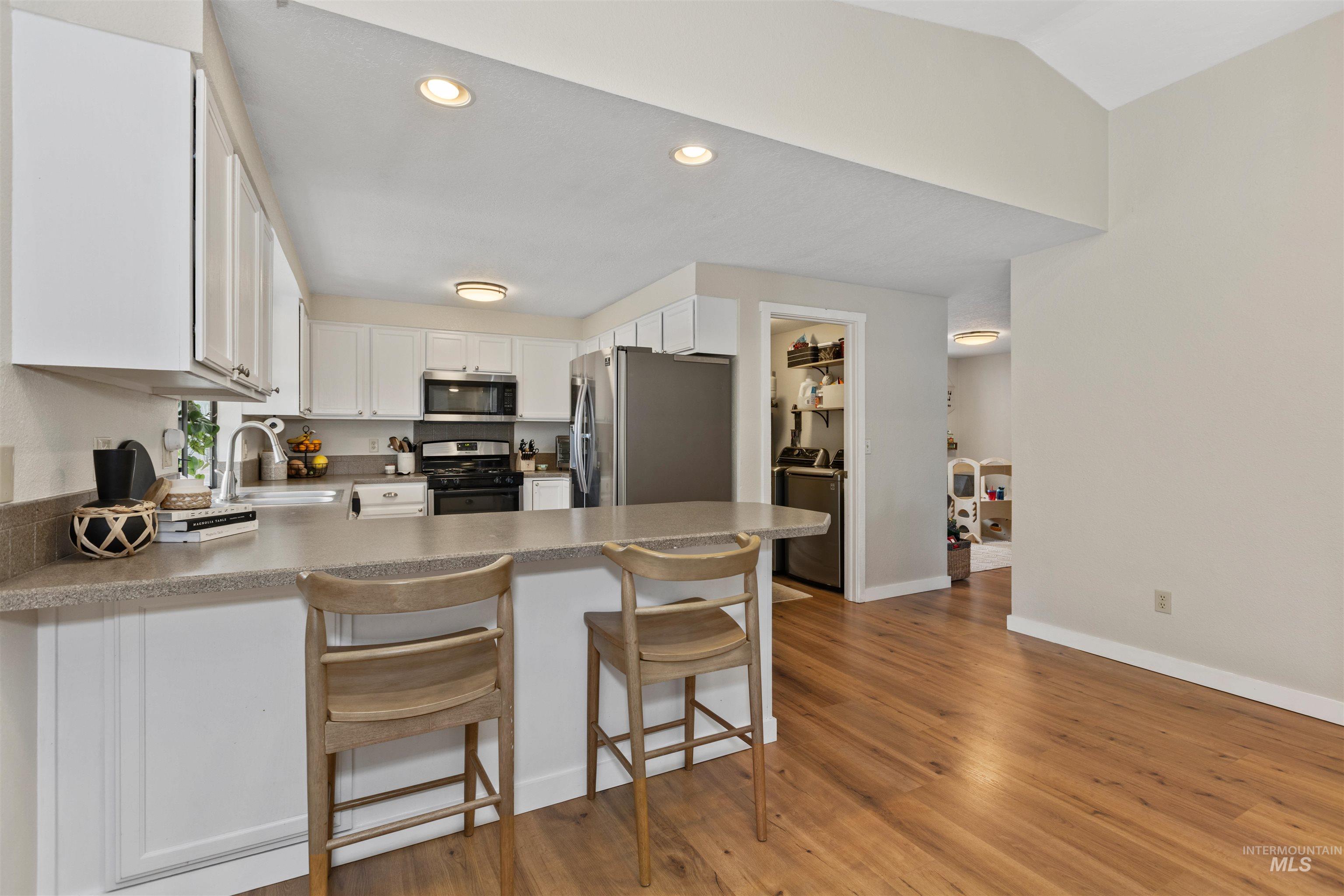 Kitchen featuring recessed lighting, stainless steel appliances, light wood-type flooring, a peninsula, and white cabinets