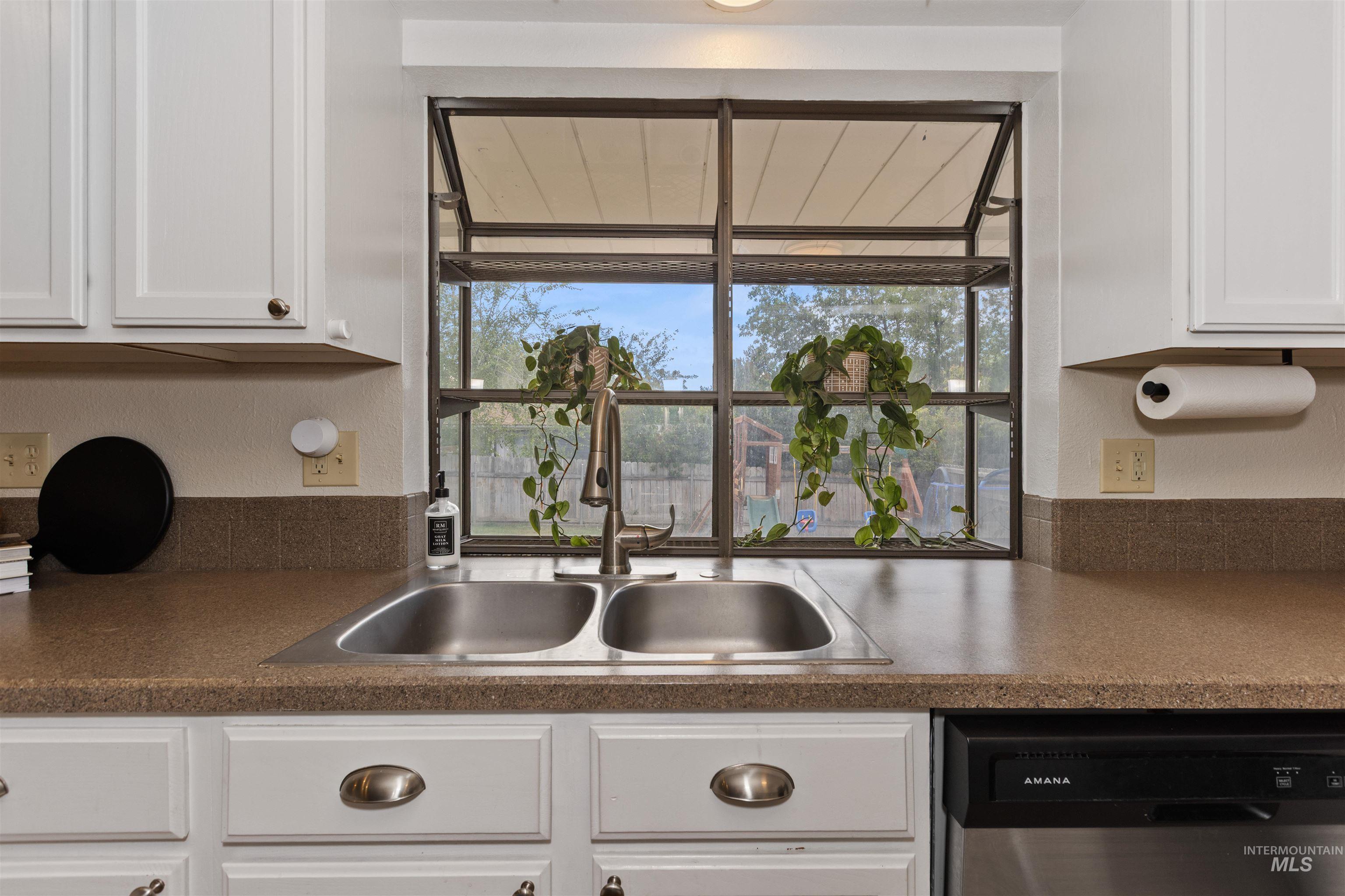 Kitchen with stainless steel dishwasher, white cabinets, dark countertops, and plenty of natural light