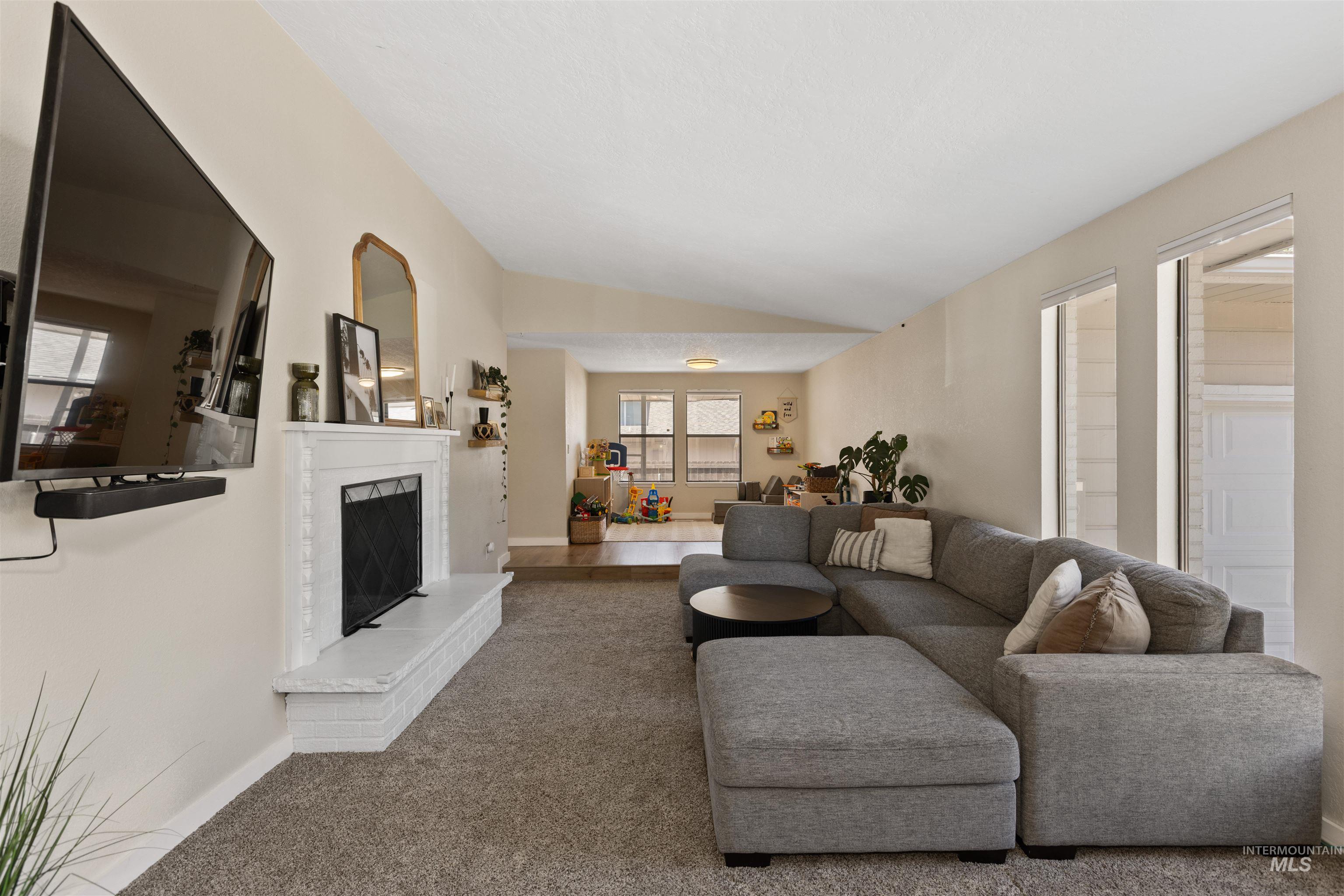 Carpeted living area featuring lofted ceiling, a fireplace, and plenty of natural light