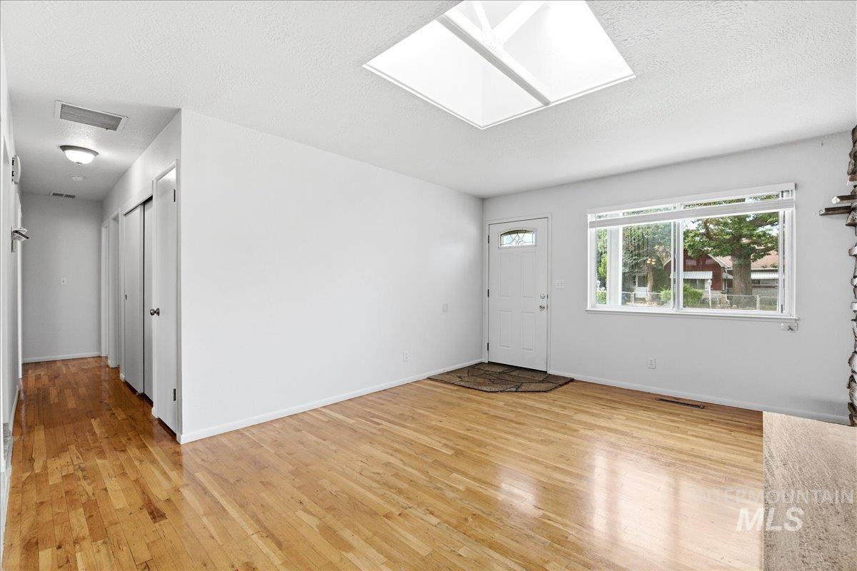 Inviting entry space featuring wood-finish flooring, a prominent skylight, a large picture window, and a white paneled entry door with decorative glass