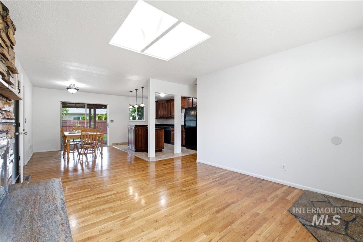 Spacious living area featuring polished wood-finish flooring, a prominent skylight, and a stone-clad fireplace