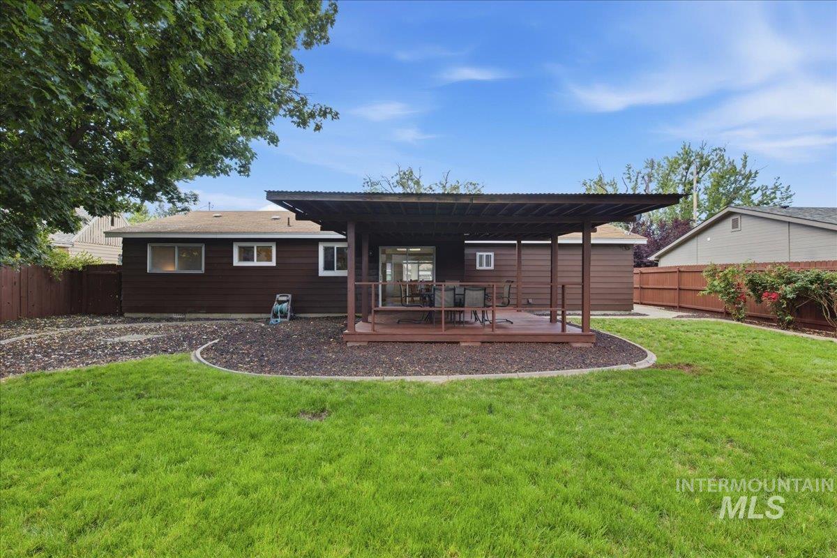 Expansive backyard featuring a manicured lawn, a raised wood deck with a covered patio, and a brown wood-paneled exterior