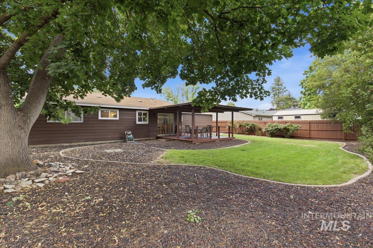 Expansive backyard with a covered patio, manicured lawn, and natural bark ground cover