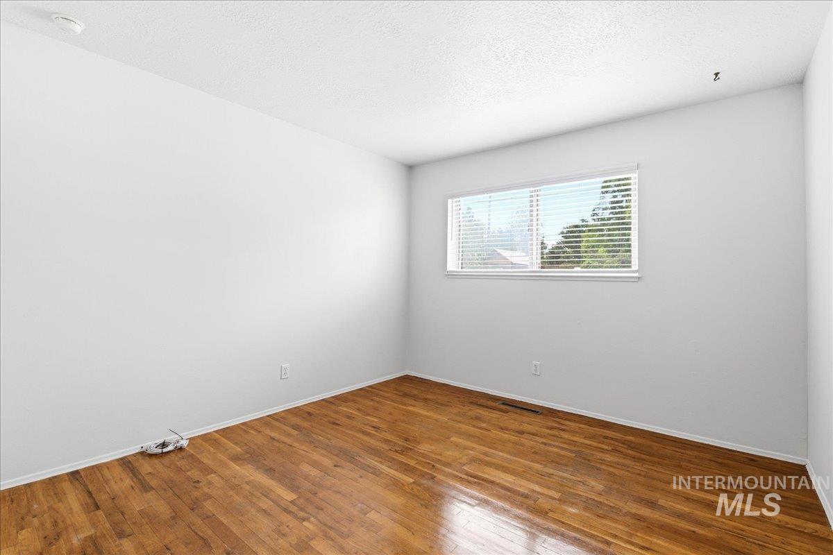 Room featuring wood-finish flooring, white baseboards, and a window with horizontal blinds