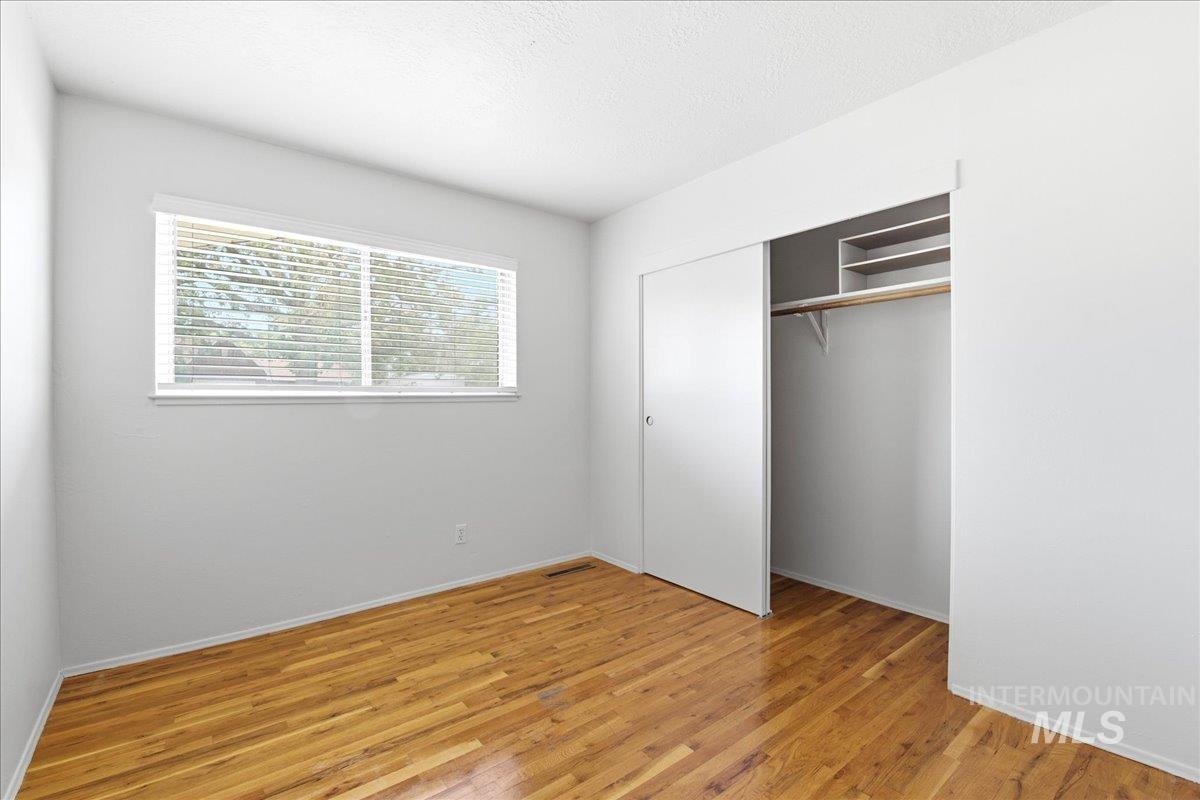 Spacious room featuring wood-finish flooring, a large window with horizontal blinds, and a closet with sliding doors and built-in shelving
