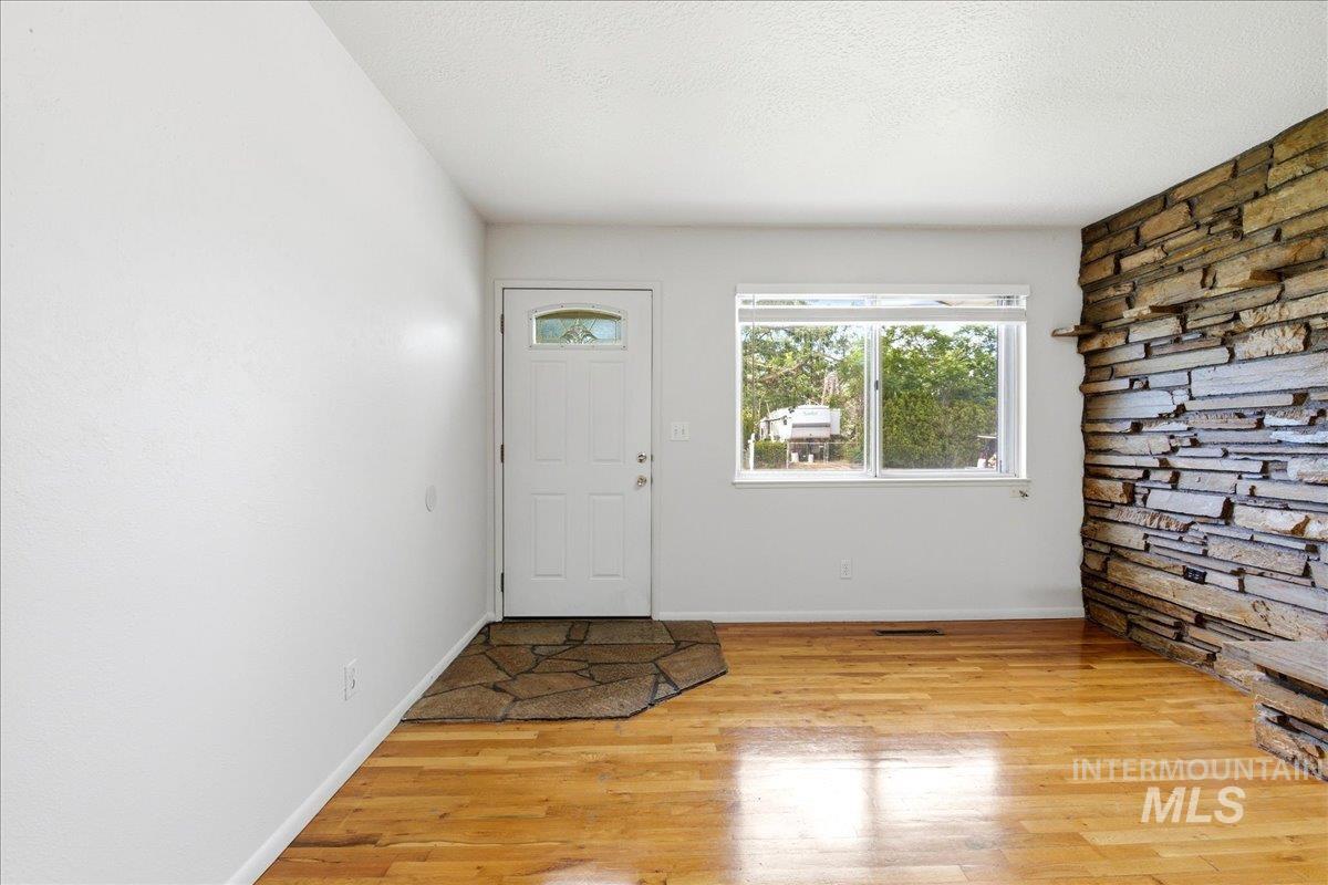 Entryway featuring wood-finish flooring, a white paneled door with an arched glass insert, a stone-tiled accent wall, and a large window with white blinds