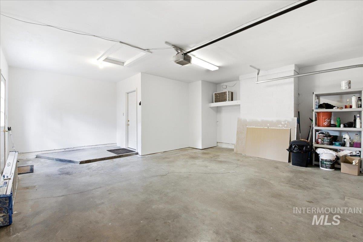Spacious garage with concrete flooring, fluorescent lighting, and a white interior door