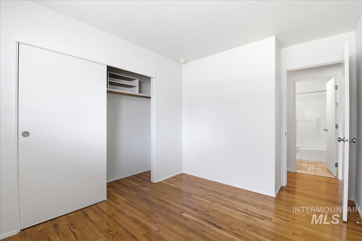 Room featuring wood-finish flooring, white walls, and a sliding door closet with internal shelving