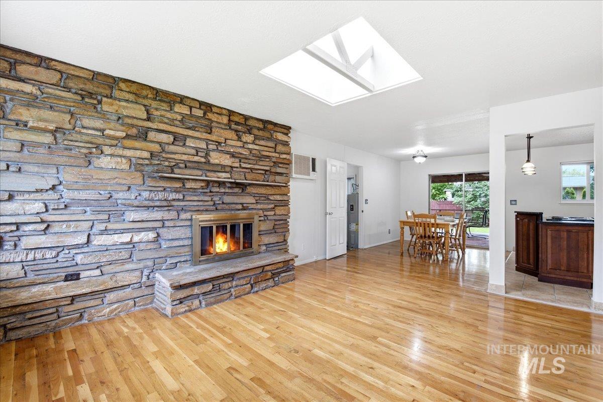 Spacious interior featuring a stacked stone fireplace with a raised hearth, wood-finish flooring, a ceiling skylight, and a sliding glass door