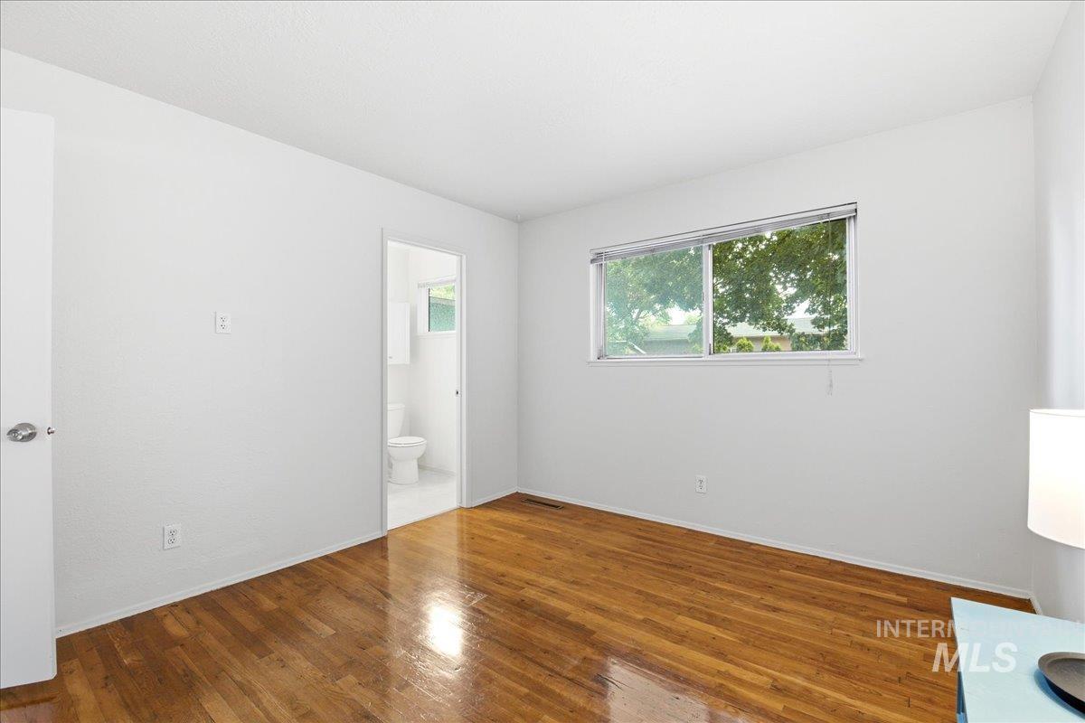 Bright interior room featuring wood-finish flooring, white walls, and a large window overlooking lush greenery