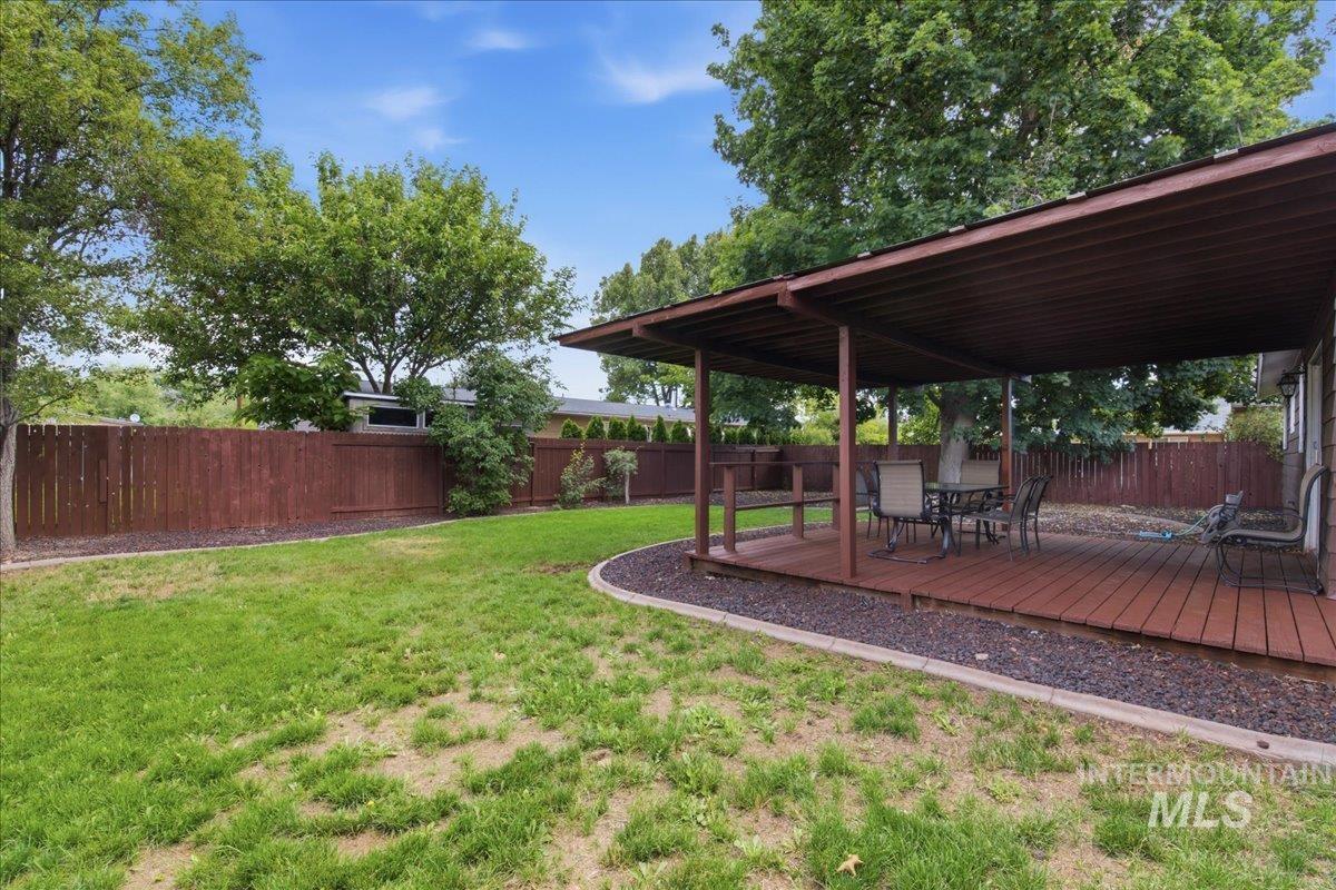 Expansive backyard featuring a covered patio with a wood-finish deck, surrounded by a privacy fence