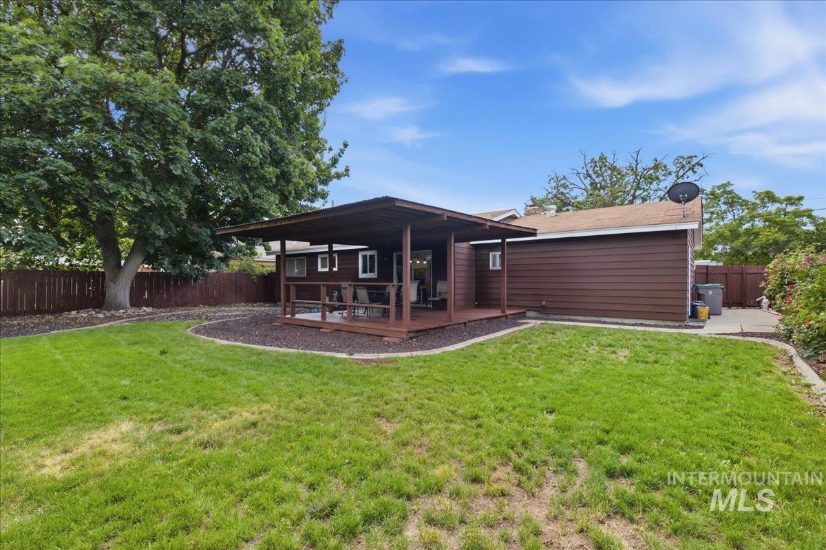Spacious backyard featuring an expansive lawn, a large covered deck, and mature trees