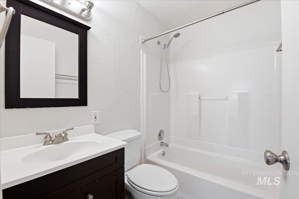 Bathroom featuring a white vanity top with an integrated sink, a dark wood-finish vanity cabinet, a framed mirror, a chrome light fixture, and a white tub with a shower combo