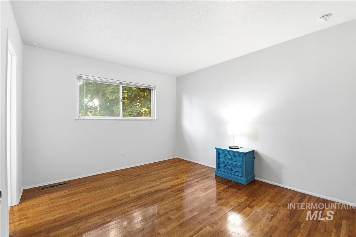 Hardwood flooring spanning the room, white walls, and a window with outdoor tree foliage
