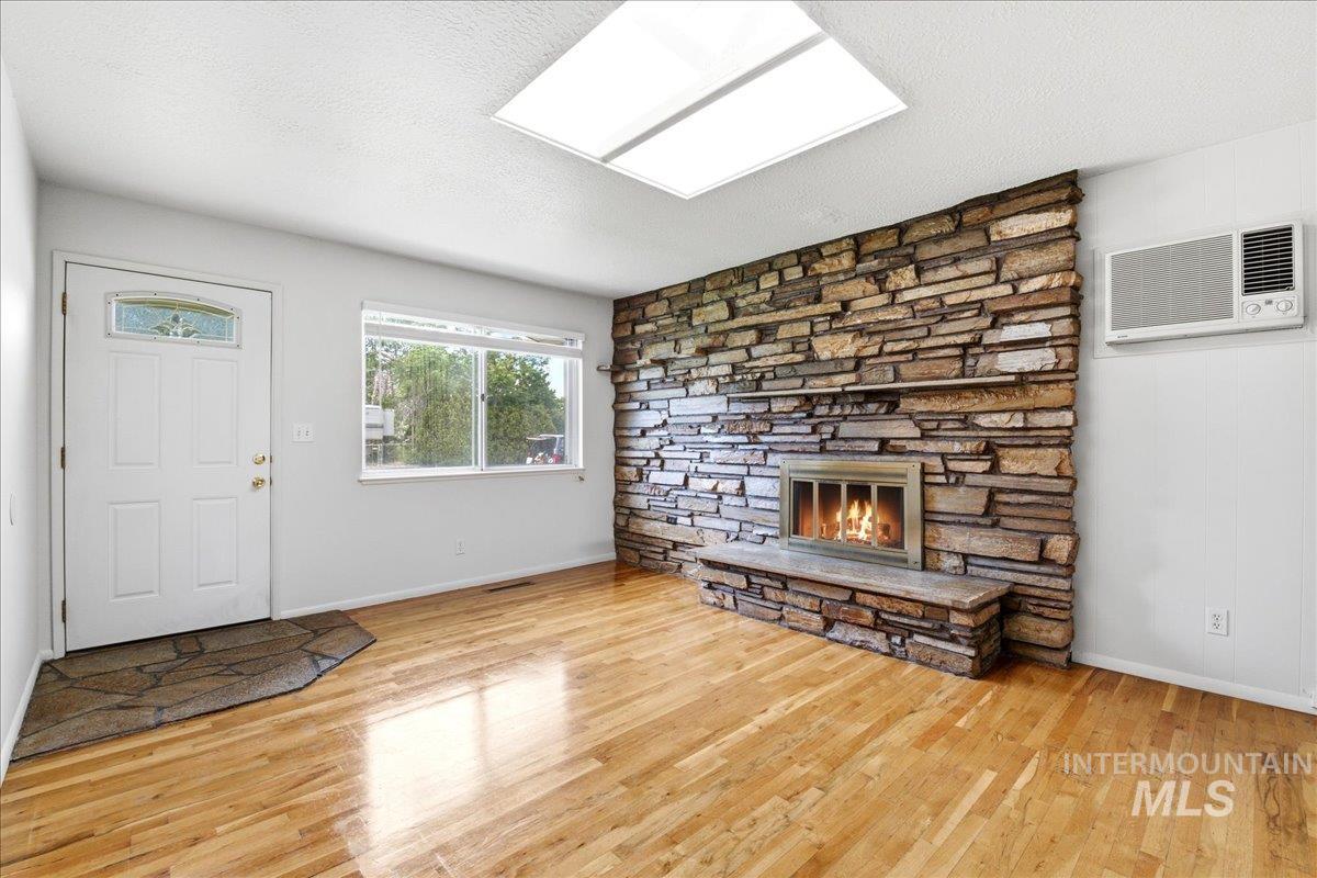 Living area featuring a stone accent wall with a fireplace, wood-finish flooring, a decorative entry door, and a skylight