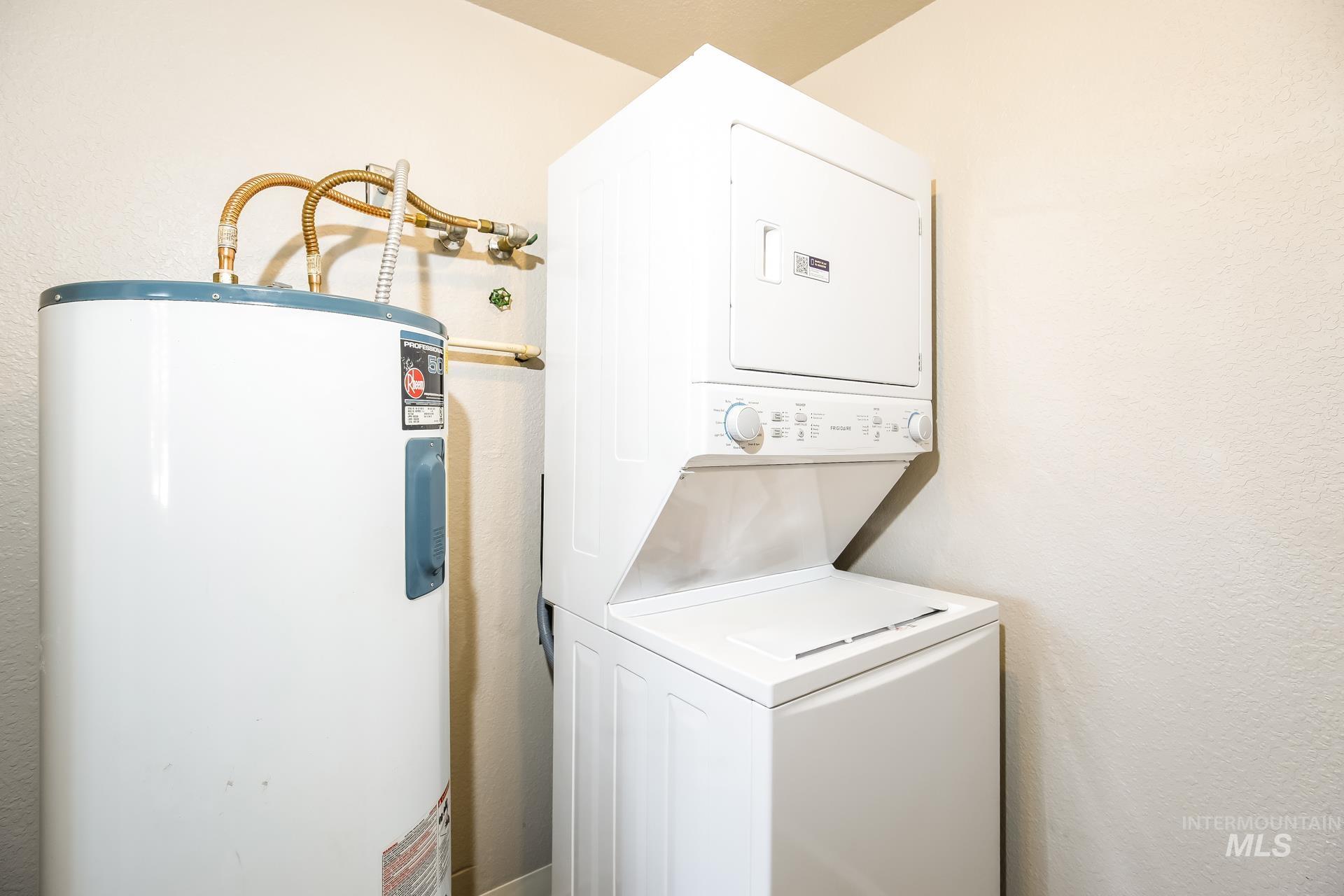 Washroom with water heater, a textured wall, and estacked washer and dryer