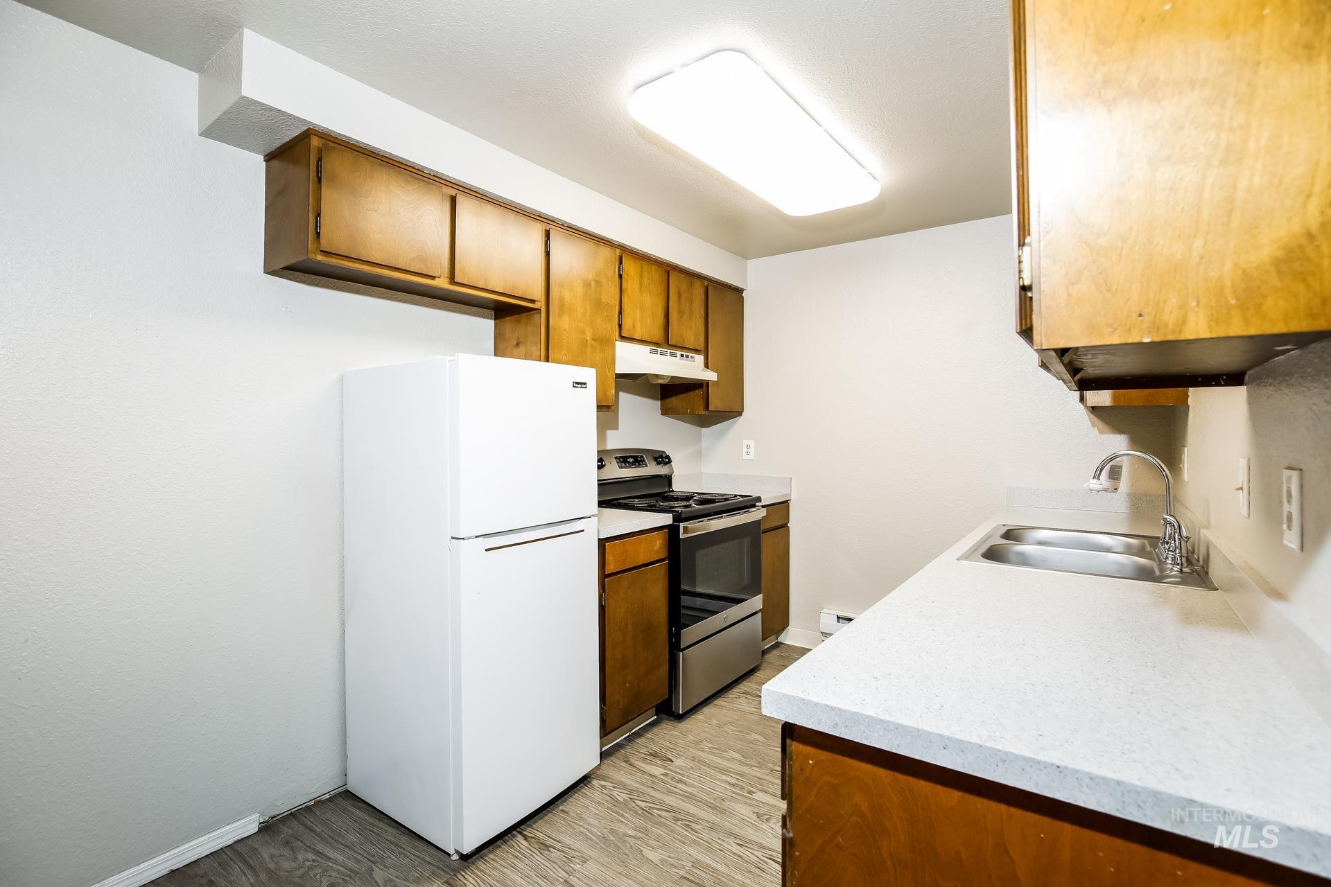 Kitchen with freestanding refrigerator, brown cabinetry, electric range, light countertops, and light wood-style floors