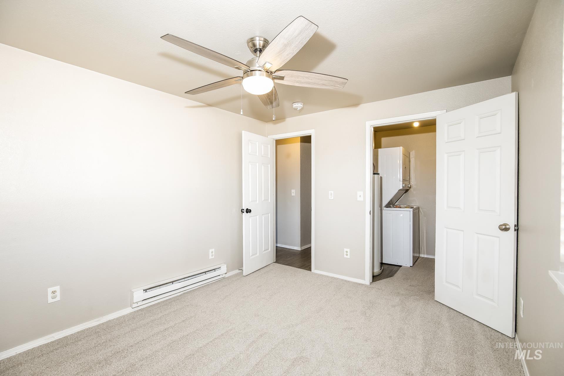 Unfurnished bedroom featuring a baseboard radiator, light carpet, ceiling fan, and washer / clothes dryer