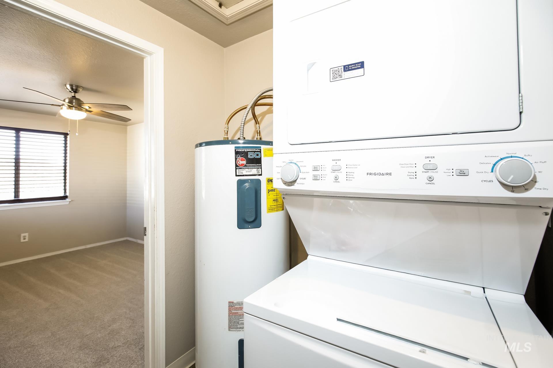 Laundry area featuring electric water heater, carpet, stacked washing machine and dryer, and a ceiling fan