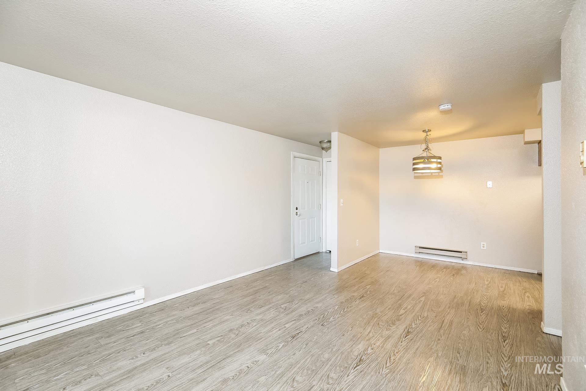 Empty room featuring wood finished floors, a baseboard radiator, and a textured ceiling