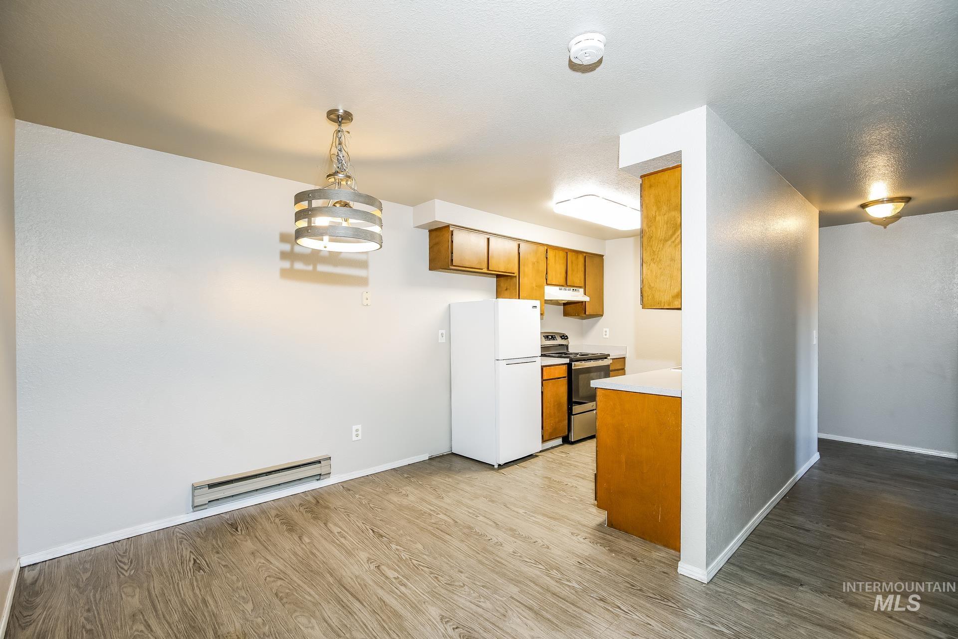 Kitchen with brown cabinets, freestanding refrigerator, light wood finished floors, light countertops, and stainless steel electric stove
